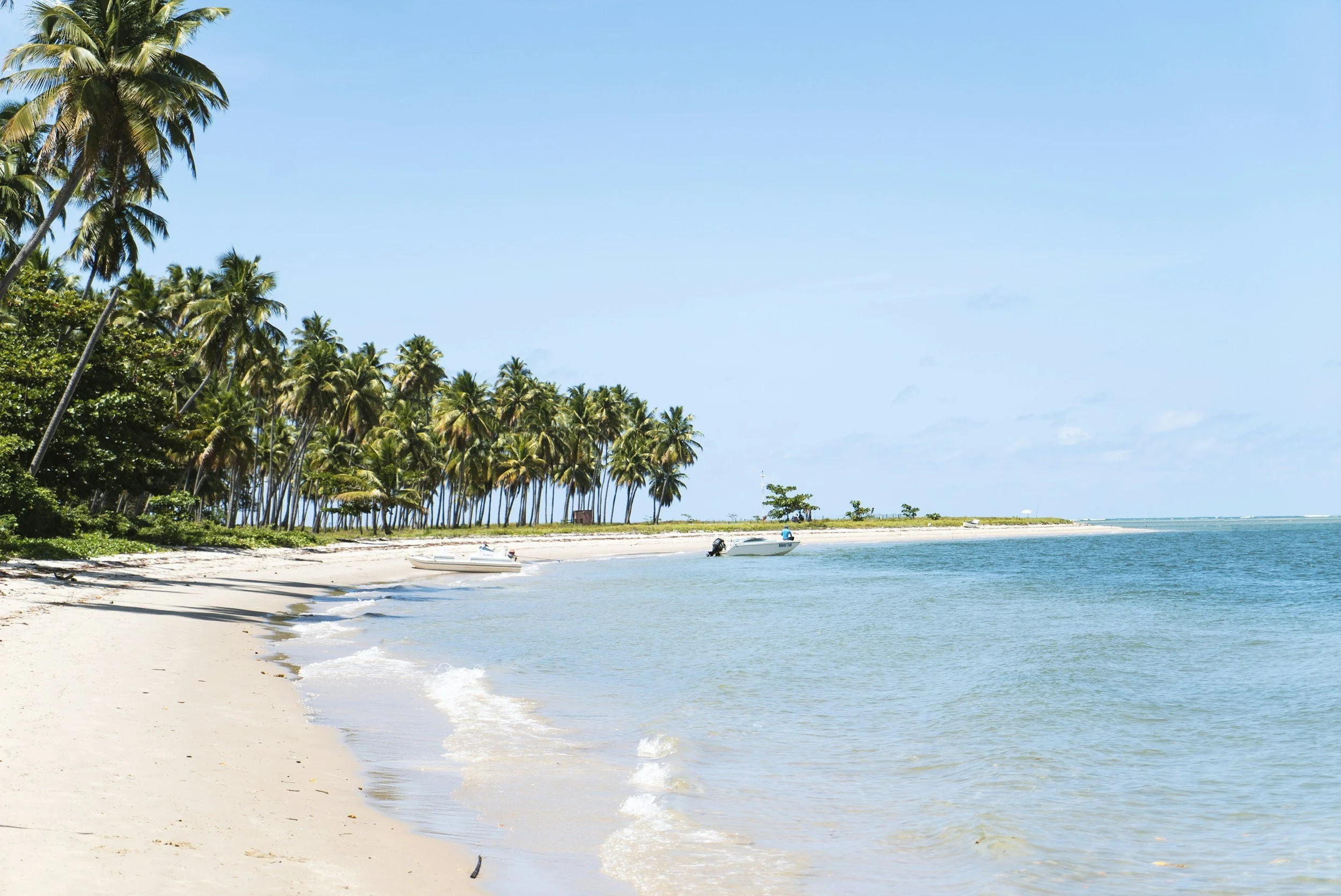 Empty palm-lined beach with small fishing boats moored in calm turquoise water on the undiscovered northwest coast of Brazil