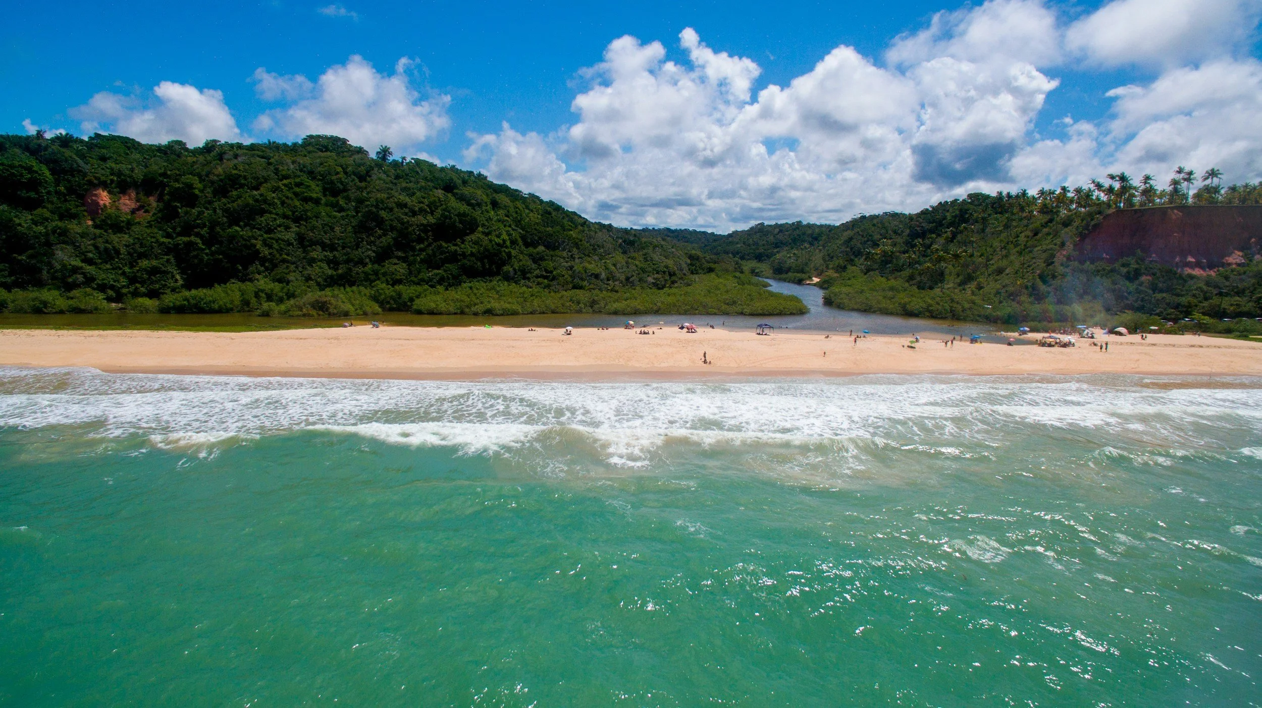 Aerial view of a river meeting the ocean along a forested coastline with white sand beaches in Bahia, Brazil