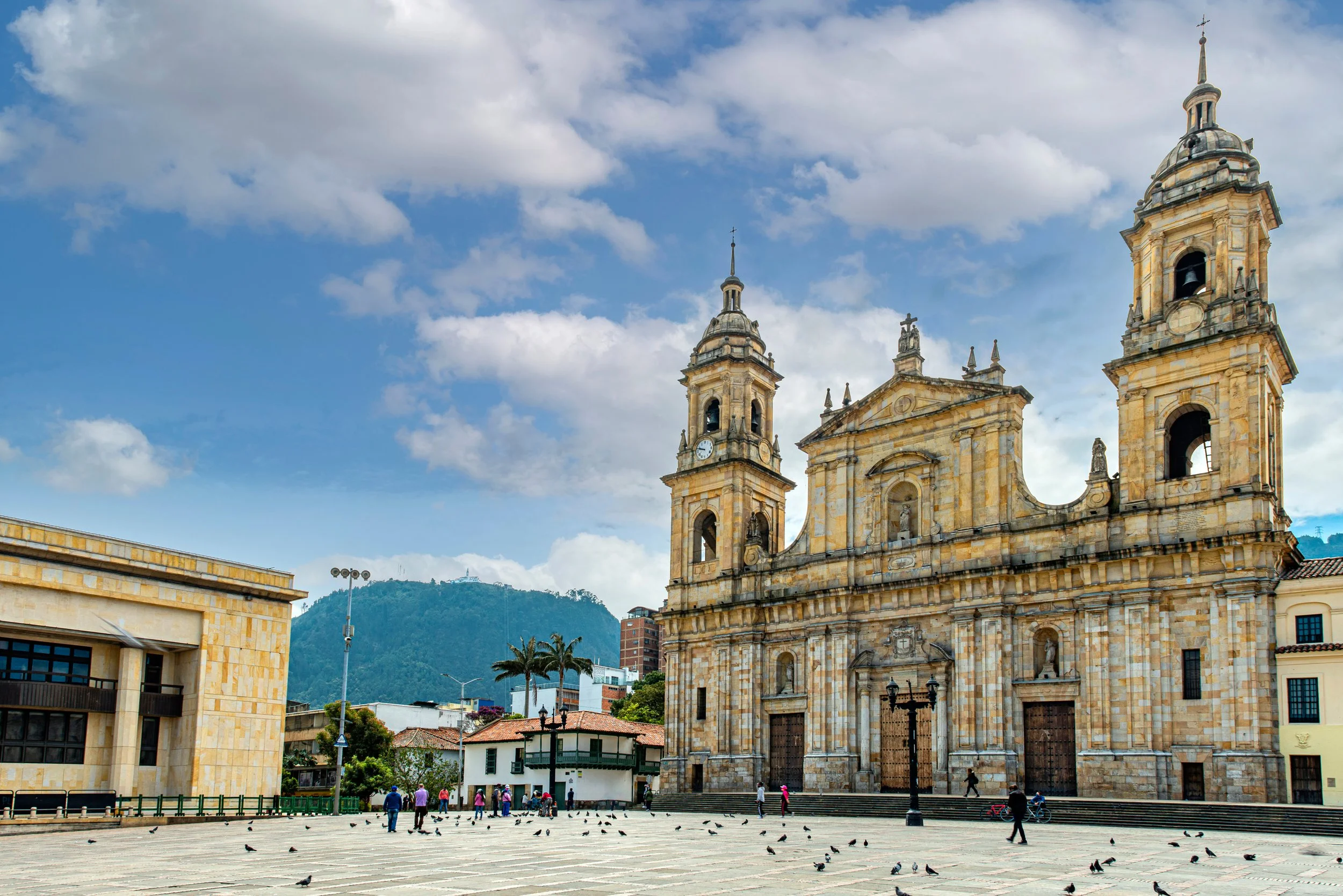 Stately stone facade and twin bell towers of the Catedral Primada overlooking Plaza de Bolívar in Bogotá, Colombia, with Andean hills behind