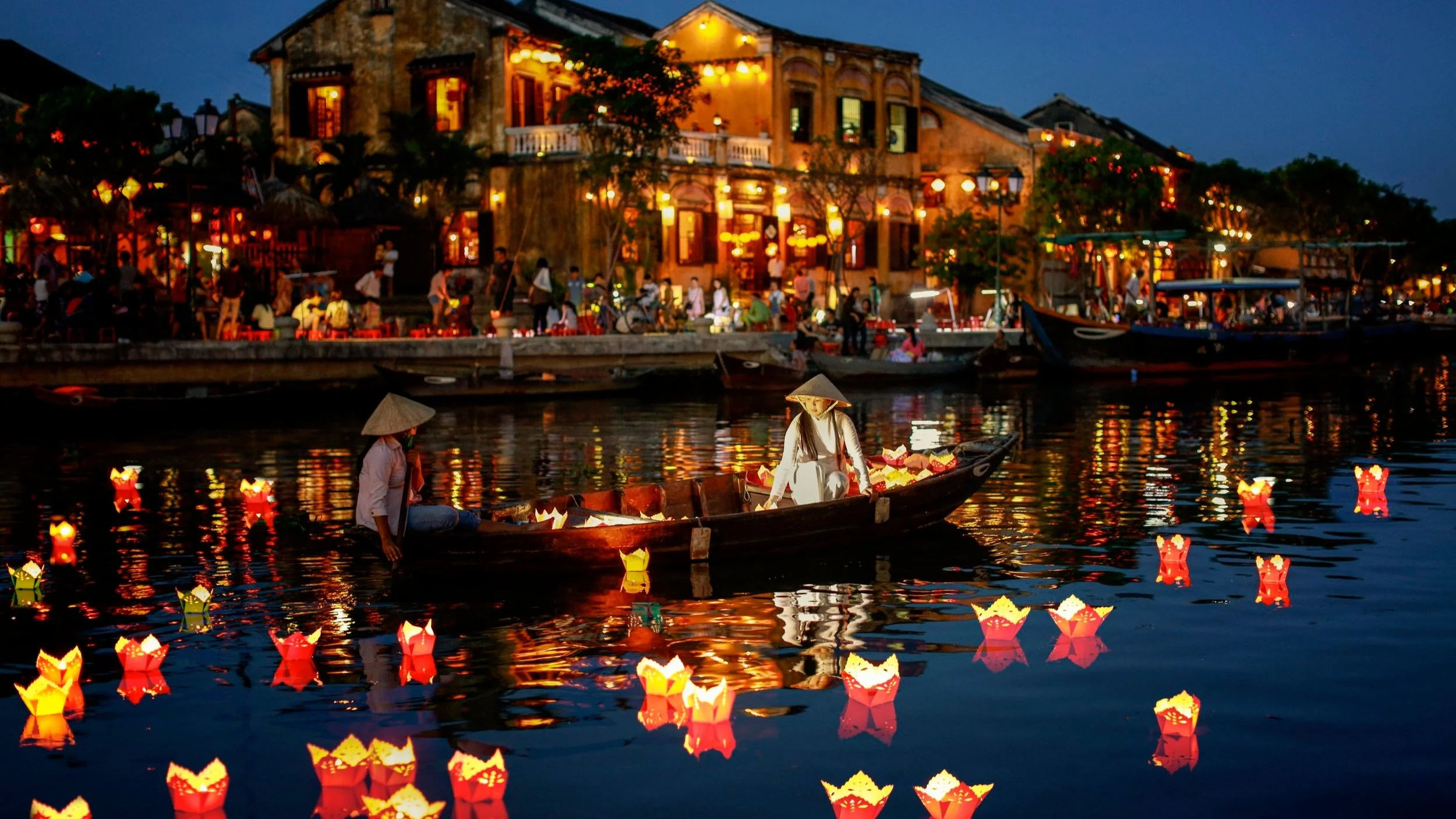 Hoi An ancient town at night with colourful paper lanterns floating on the Thu Bon River, wooden boats and illuminated historic merchant houses reflected in the dark water, Vietnam