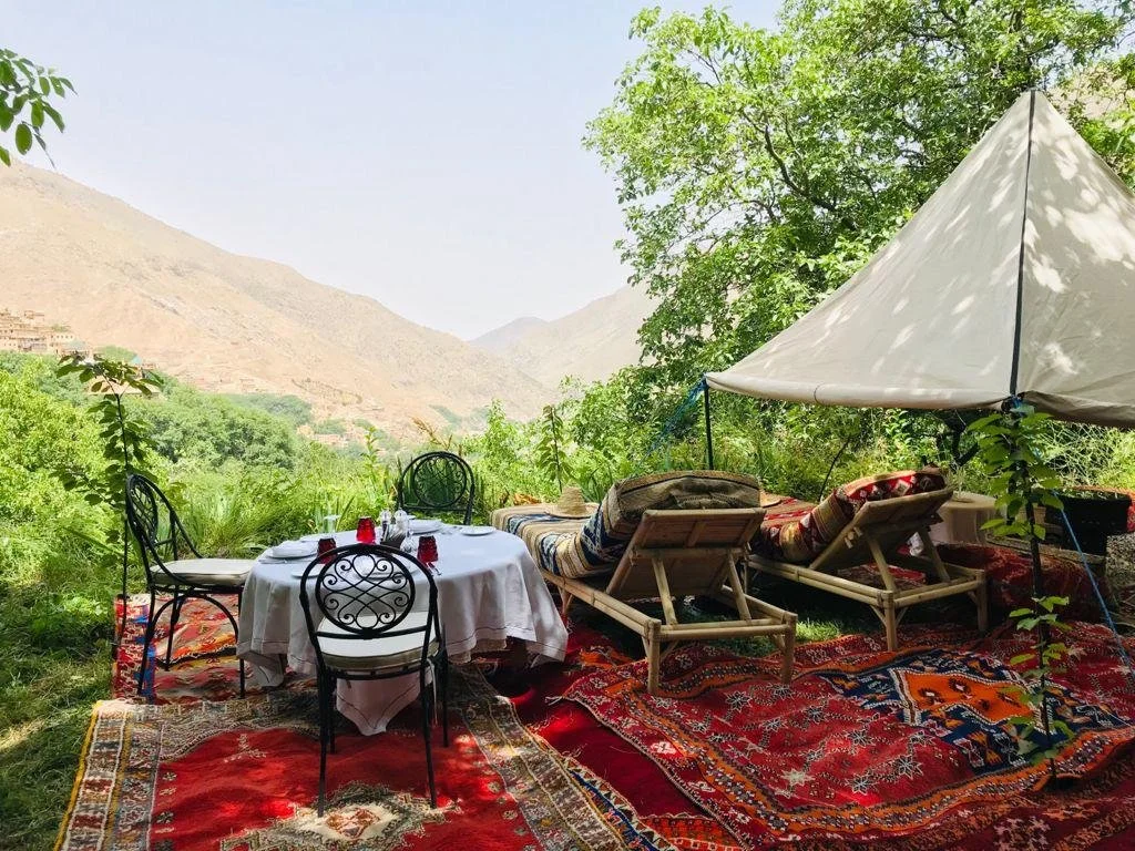 Private picnic set up with Berber rugs and a white tent in a green valley in the High Atlas Mountains
