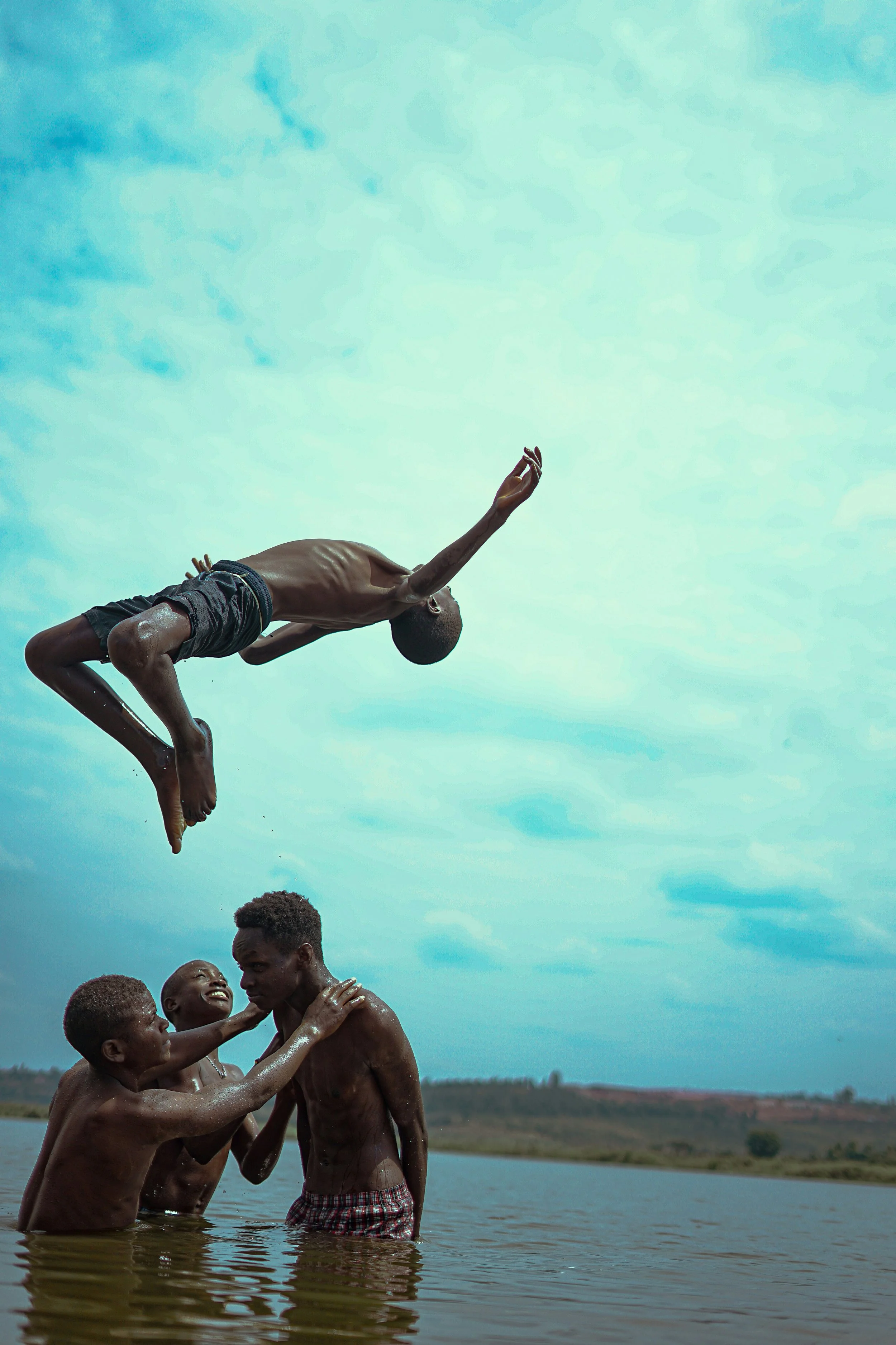 Young Rwandan acrobat performing a backflip high in the air above a companion against a bright blue sky in Kigali, Rwanda