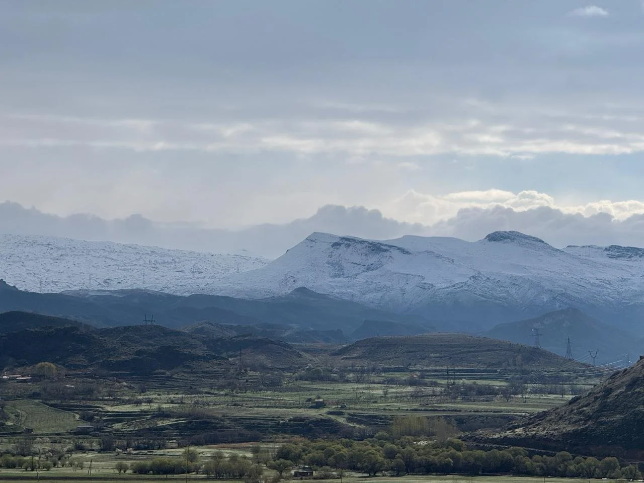 Expansive view across the Ararat Valley wine region in Armenia with green patchwork fields in the foreground and snow-covered mountain ranges stretching across the horizon