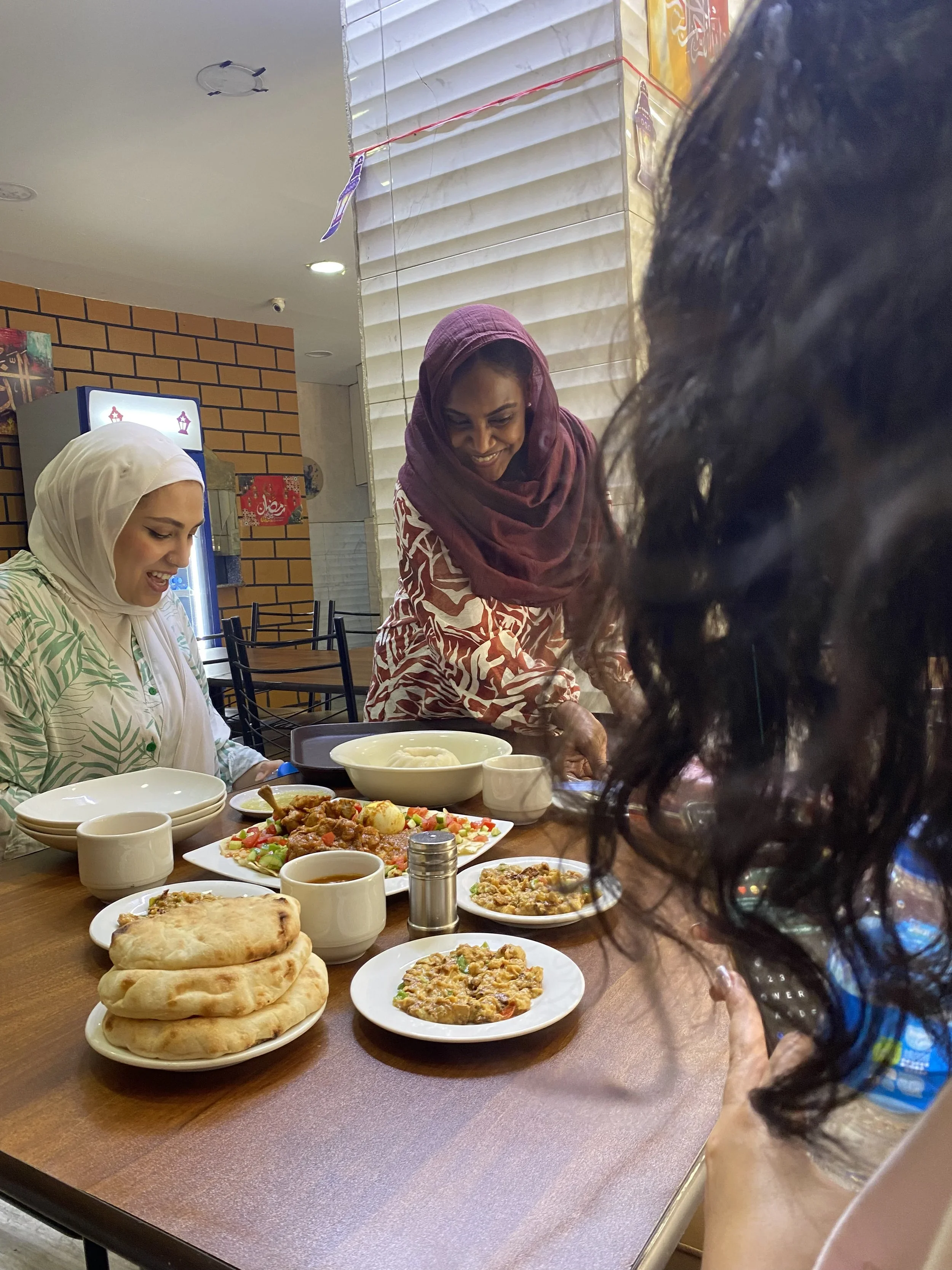 Two Egyptian women in headscarves sharing a meal of traditional flatbreads and mezze dishes at a local Cairo restaurant, Egypt