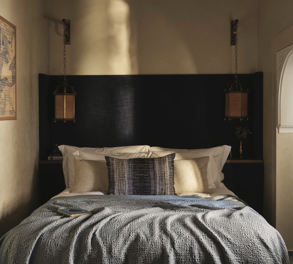 A cozy bedroom with a bed, decorative pillows, a dark headboard, pendant lights hanging from chains, and a phone resting on the bed.