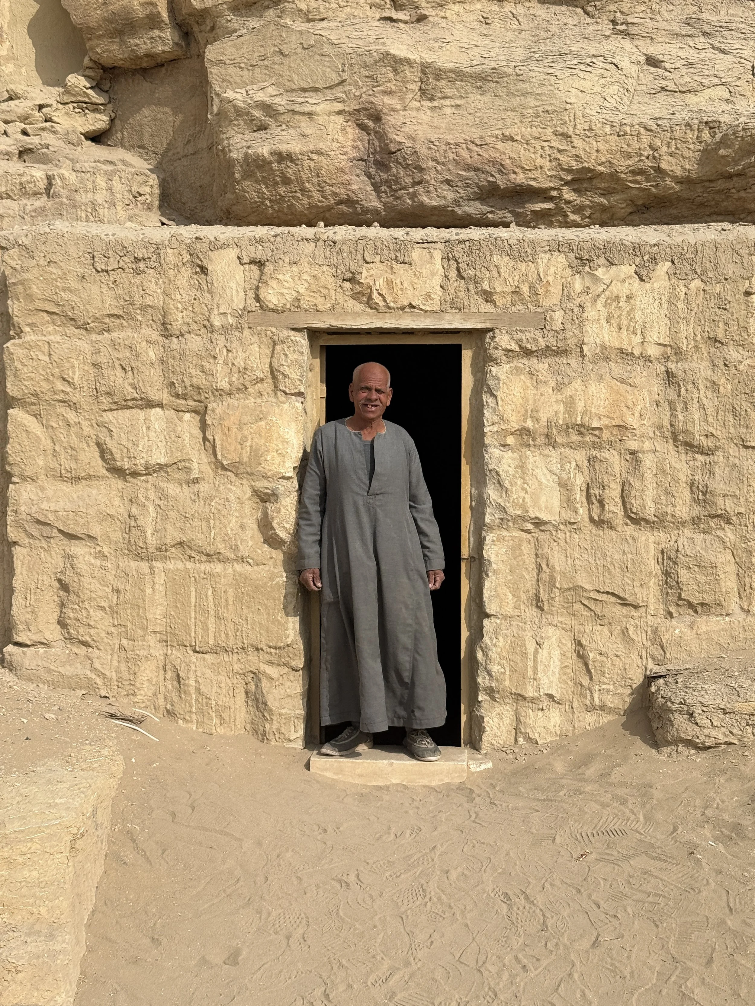 Egyptian guide standing in the stone doorway of an ancient tomb at the Saqqara necropolis near Cairo, Egypt