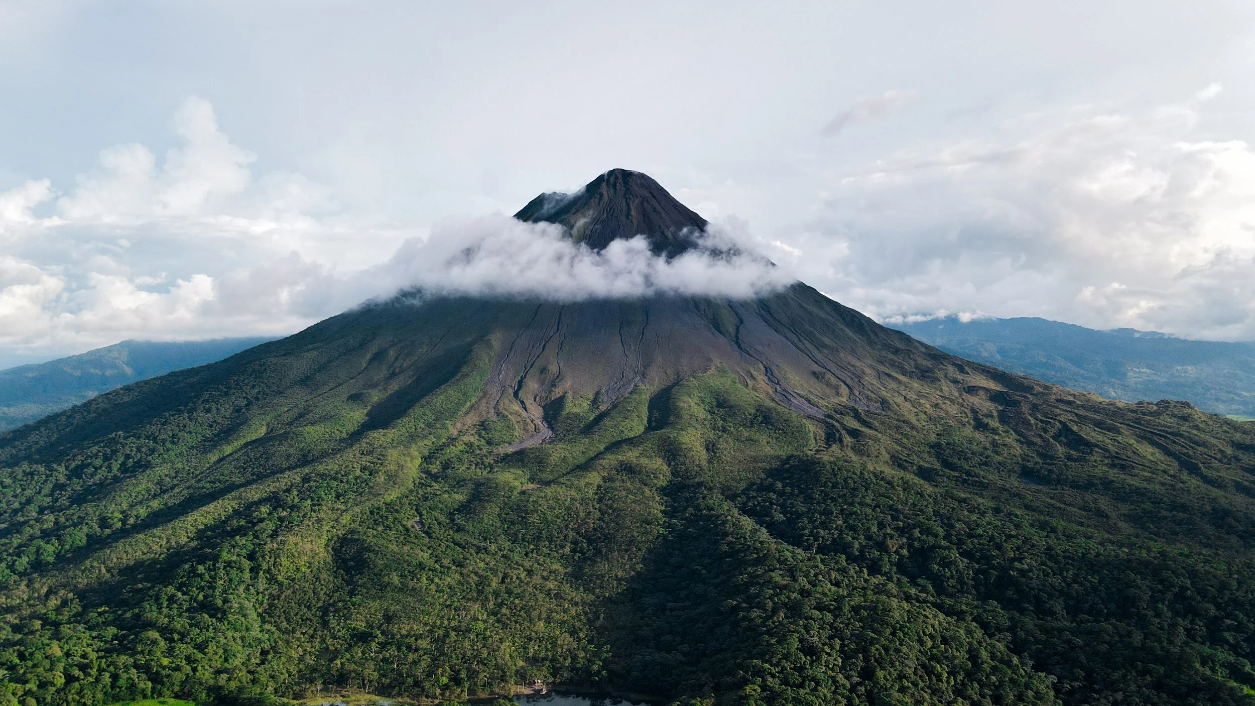 Arenal volcano cone wreathed in cloud rising above dense rainforest in northern Costa Rica