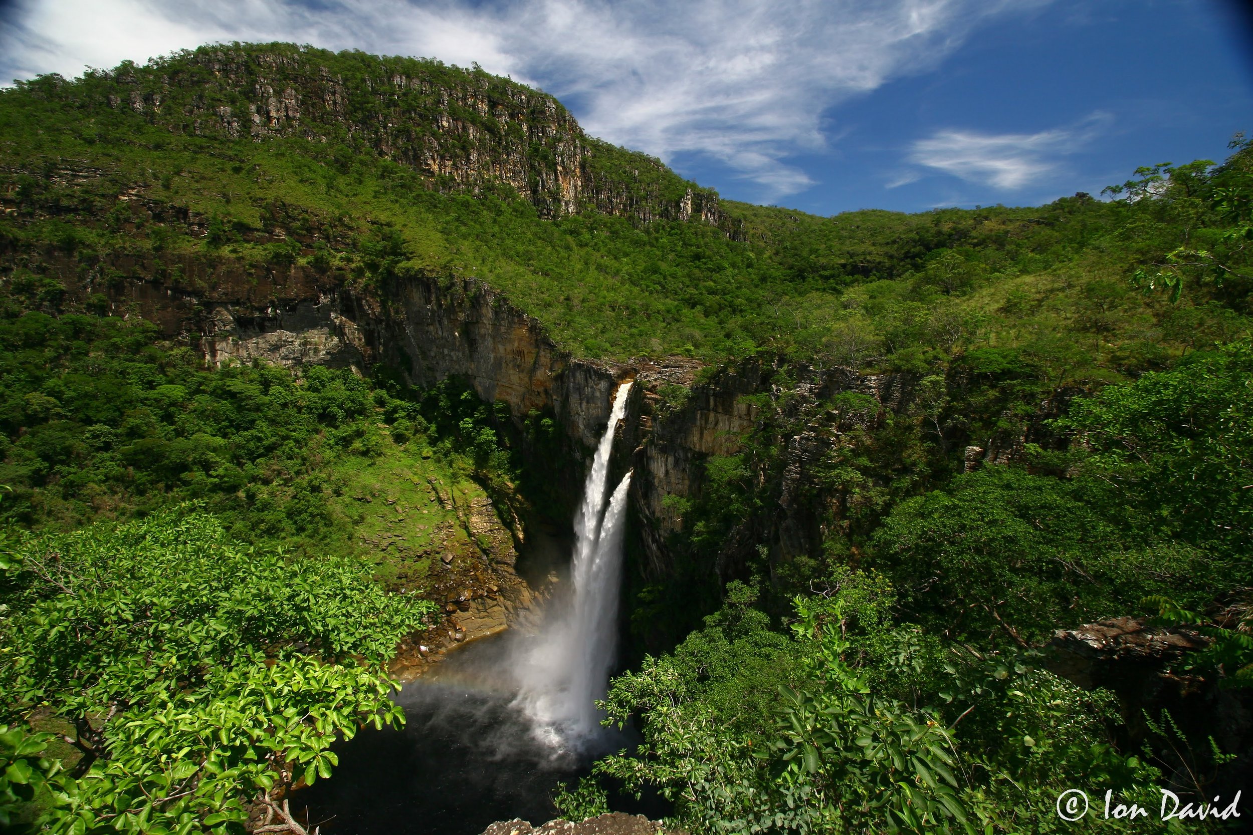 Tall waterfall plunging from a green cliff edge into a misty pool in the Cerrado savanna wilderness of Brazil