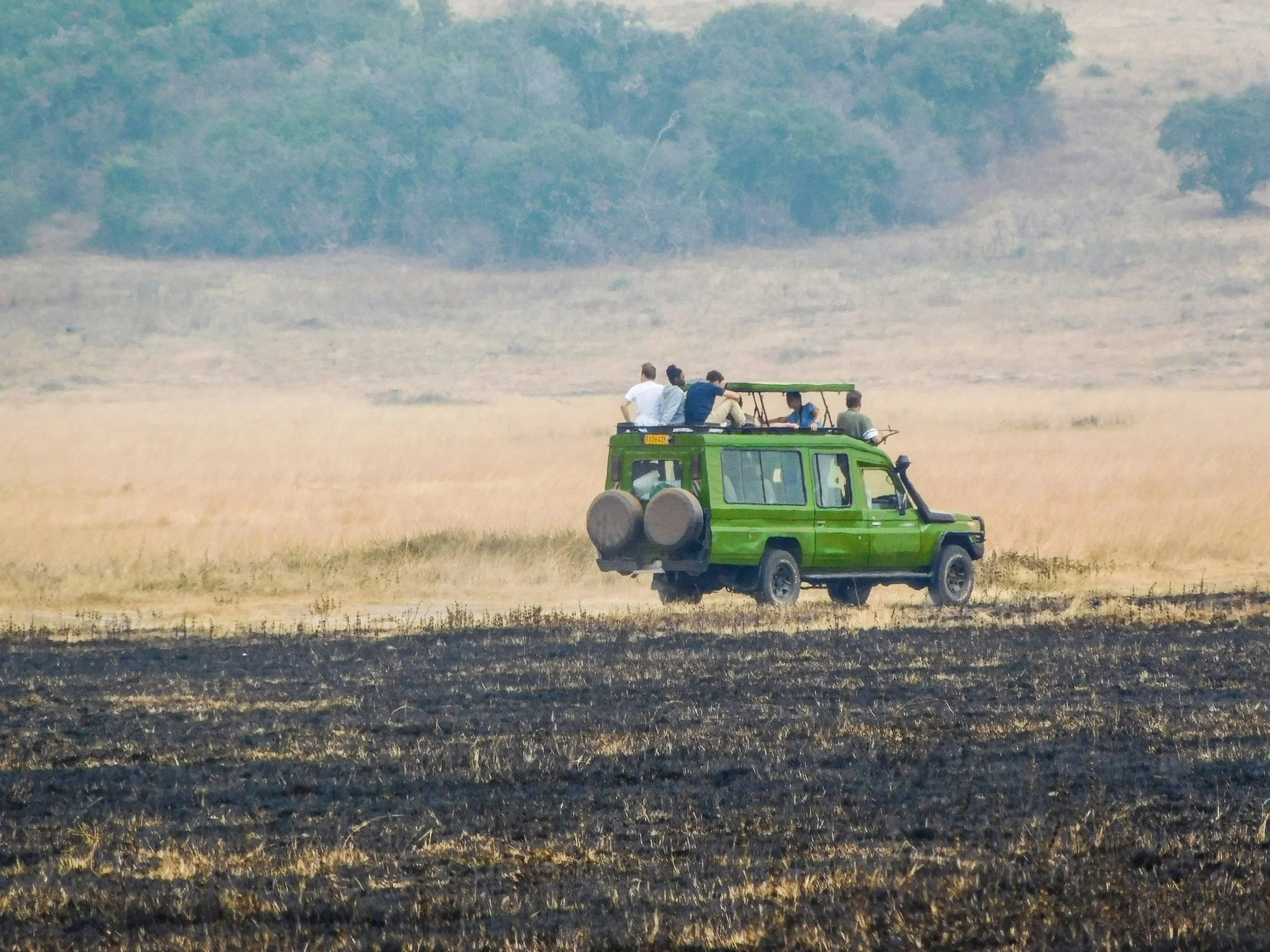 Green open-roof safari Land Cruiser driving across open golden grassland in Akagera National Park, Rwanda, with guests enjoying a Big Five game drive