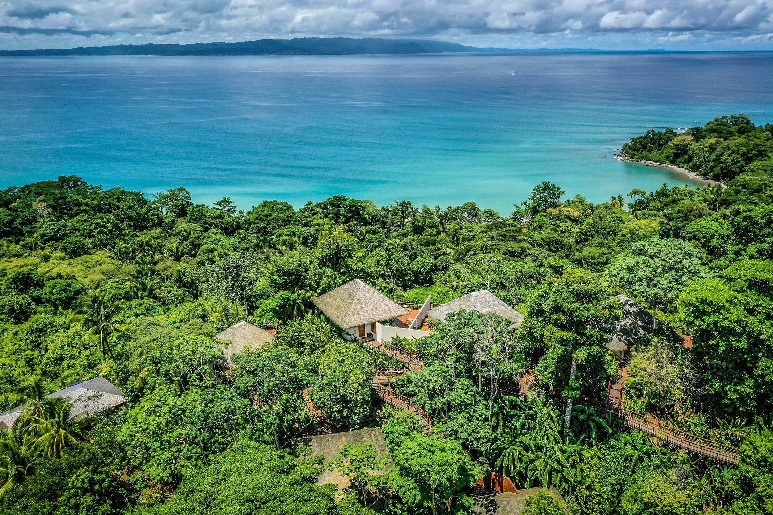 Aerial view of a thatched-roof eco lodge nestled in dense rainforest above a turquoise bay on the Osa Peninsula, Costa Rica