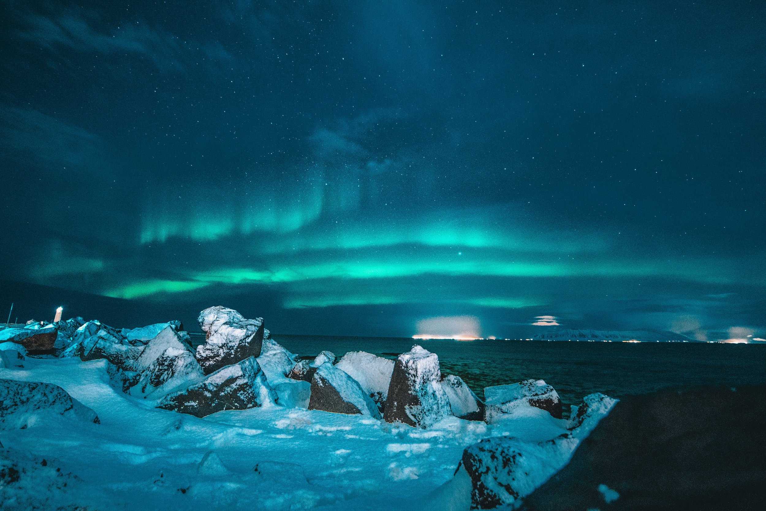 Vivid green aurora borealis dancing over a snowy Icelandic landscape at night, with ice formations in the foreground and a reflection of the Northern Lights on still water