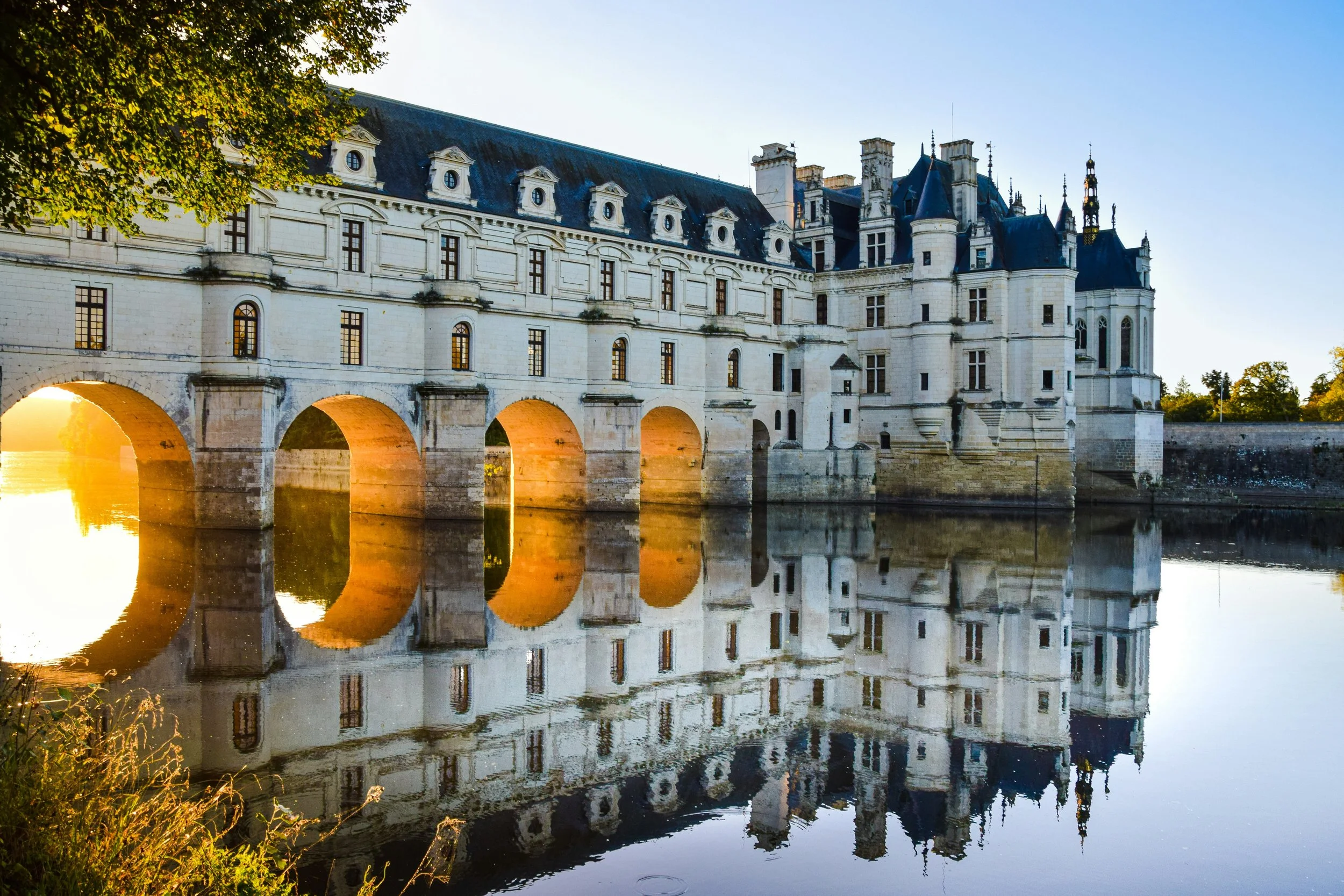 The Renaissance Château de Chenonceau spanning the River Cher at golden hour, perfectly reflected in the still water below, Loire Valley, France