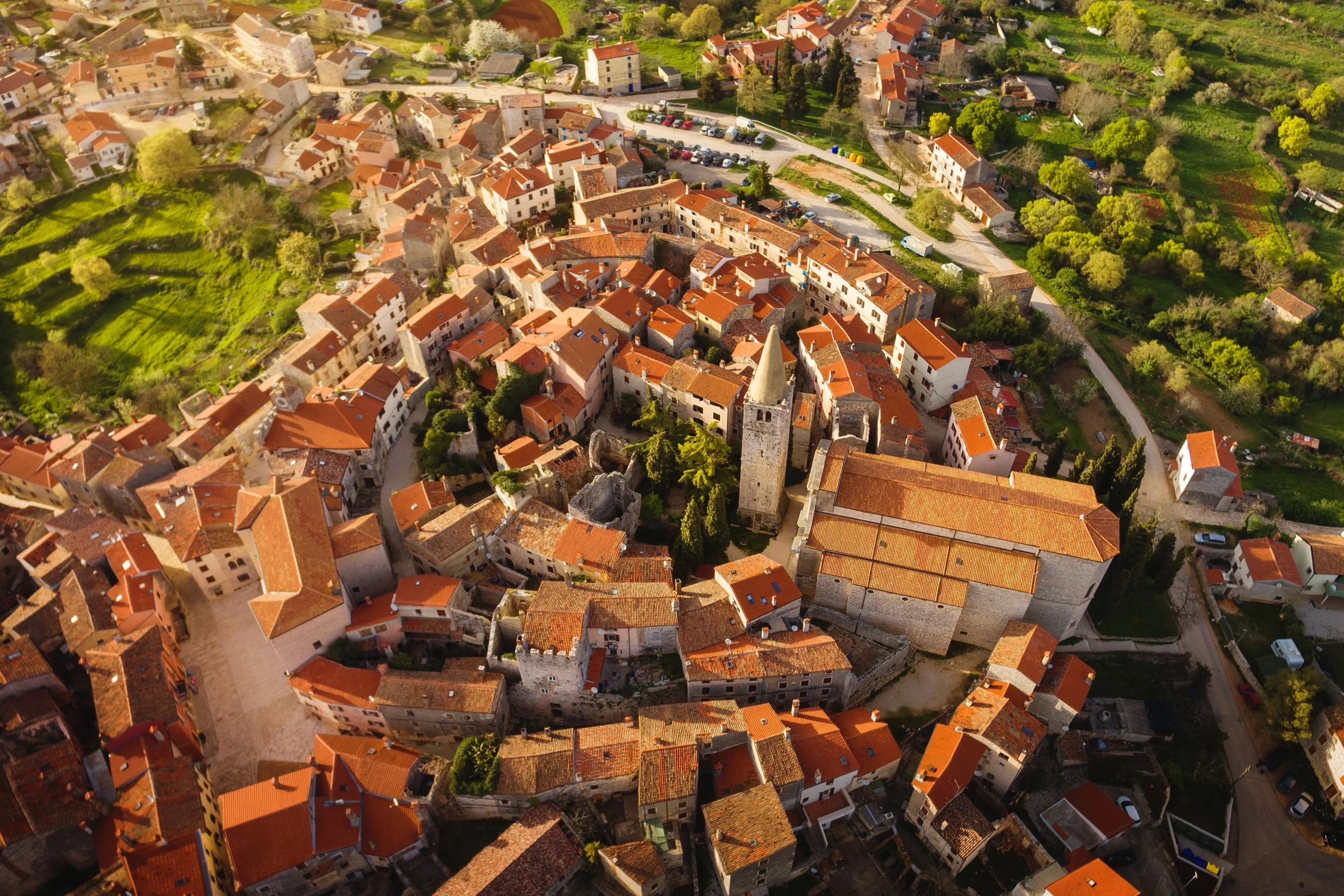 Aerial view of a circular medieval hilltop town in Istria with a Romanesque bell tower and terracotta rooftops surrounded by green countryside, Croatia
