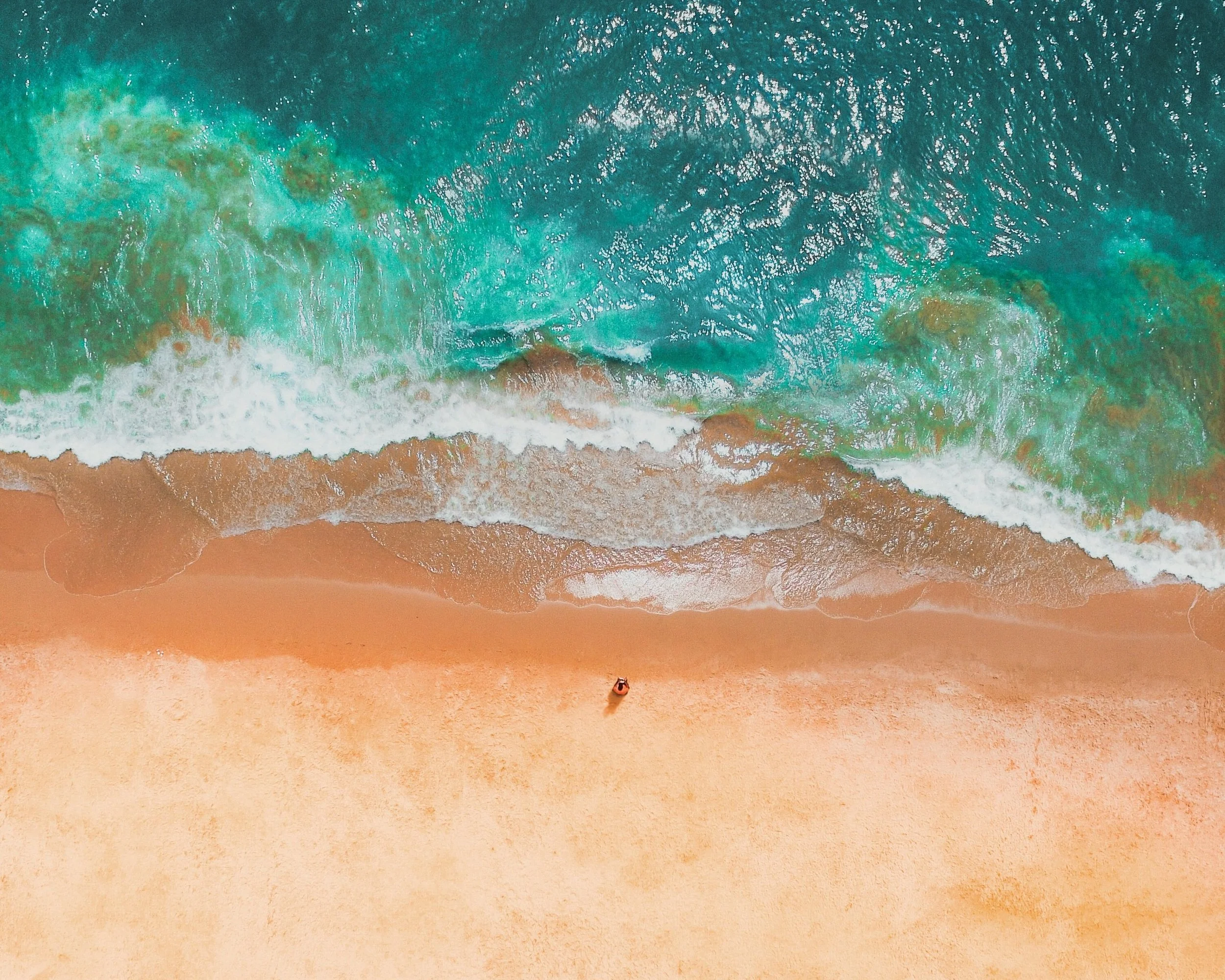 Aerial view of a pristine Algarve beach with turquoise waves washing over golden sand and a lone swimmer visible from above, southern Portugal