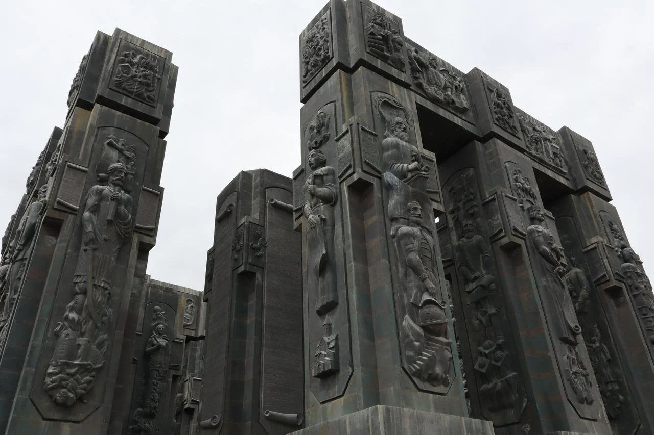 Towering dark stone columns of the Chronicles of Georgia monument in Tbilisi, carved with religious and historical reliefs depicting Georgian history and culture