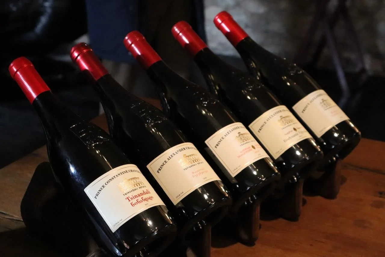 A row of dark bottles of Prince Constantine and Prince Alexander Chavchavadze Tsinandali wine with red capsules and Georgian script labels lined up on a wooden surface in Kakheti, Georgia