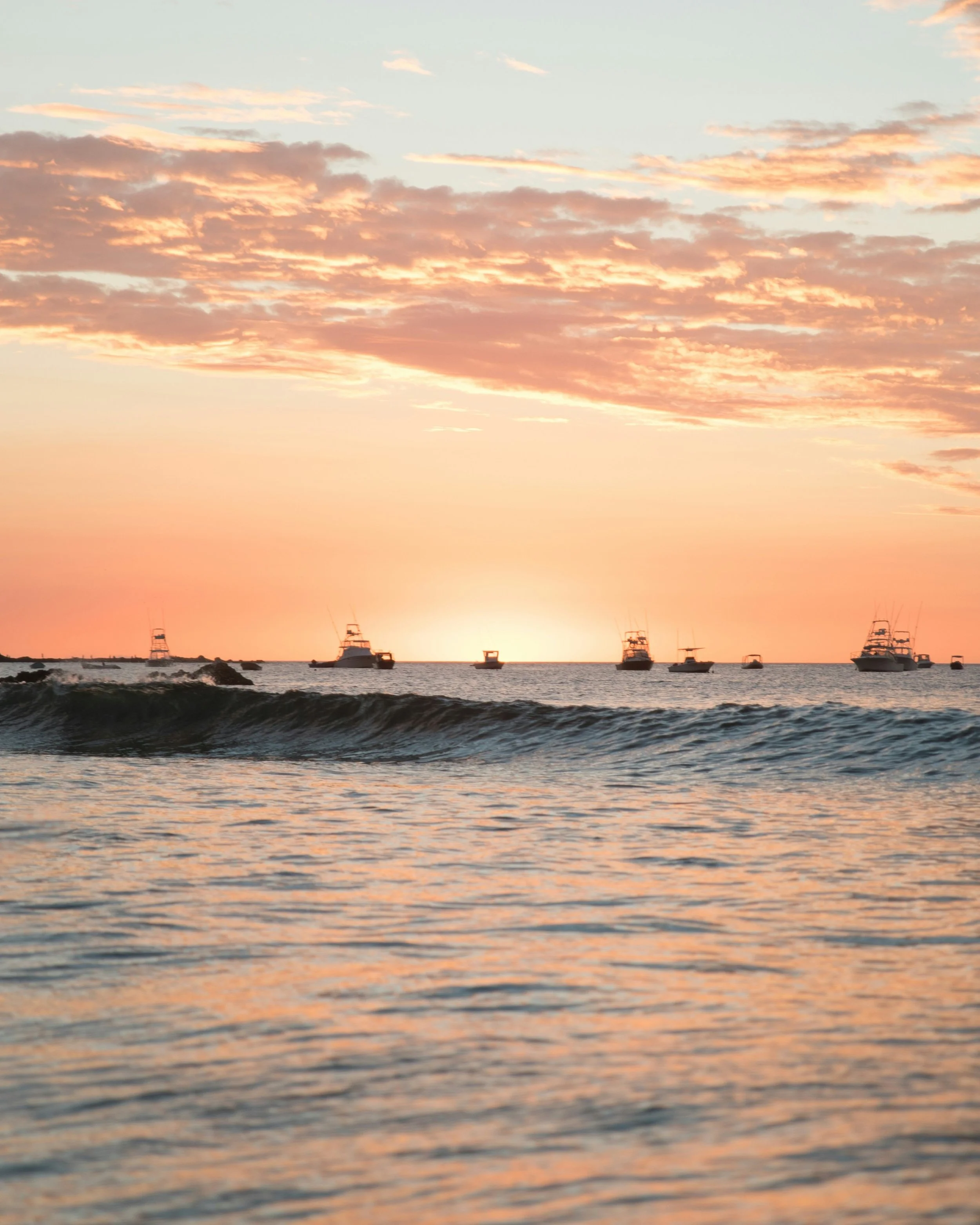 Fishing boats anchored offshore silhouetted against a glowing orange sunset over the Pacific Ocean near Península Papagayo, Costa Rica