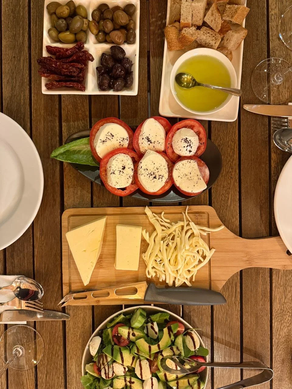 Overhead view of an Armenian wine tasting spread with stuffed peppers, local cheese, dried fruits, olive oil, and fresh greens on a wooden table