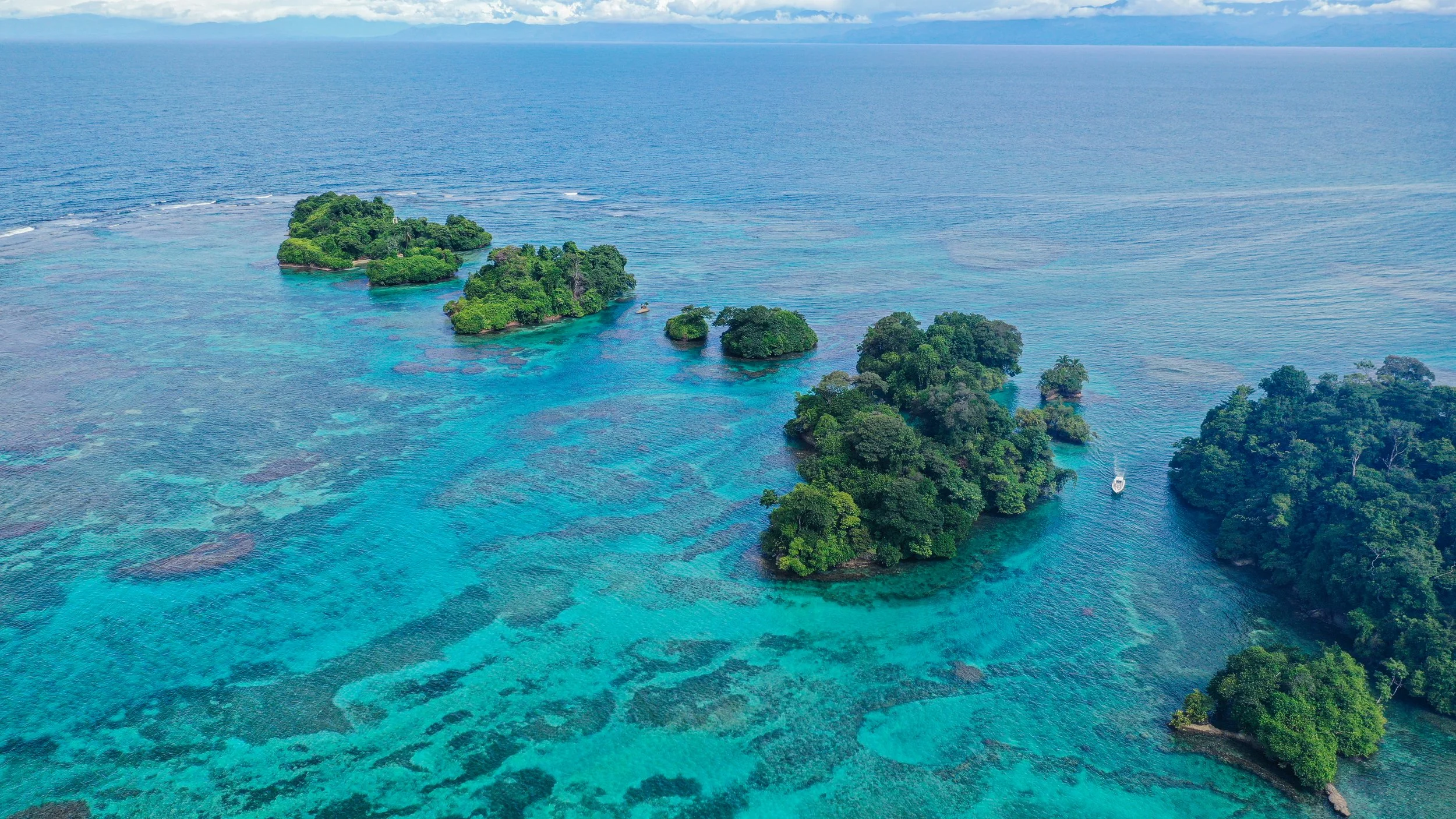 Aerial view of the lush palm-covered islands of the Bocas del Toro archipelago surrounded by turquoise Caribbean waters with coral reefs visible below, Panama