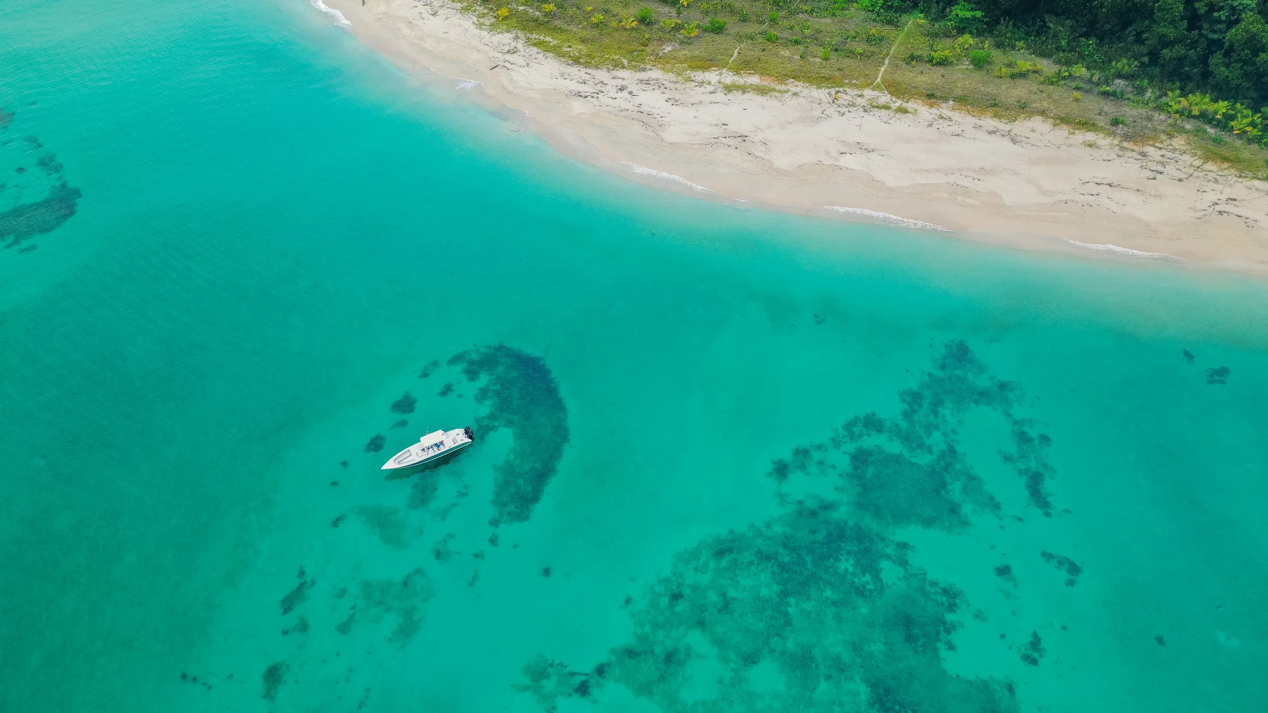 Aerial view of a private island retreat surrounded by shallow turquoise water and coral reef in the Caribbean, with a private boat moored alongside, Panama
