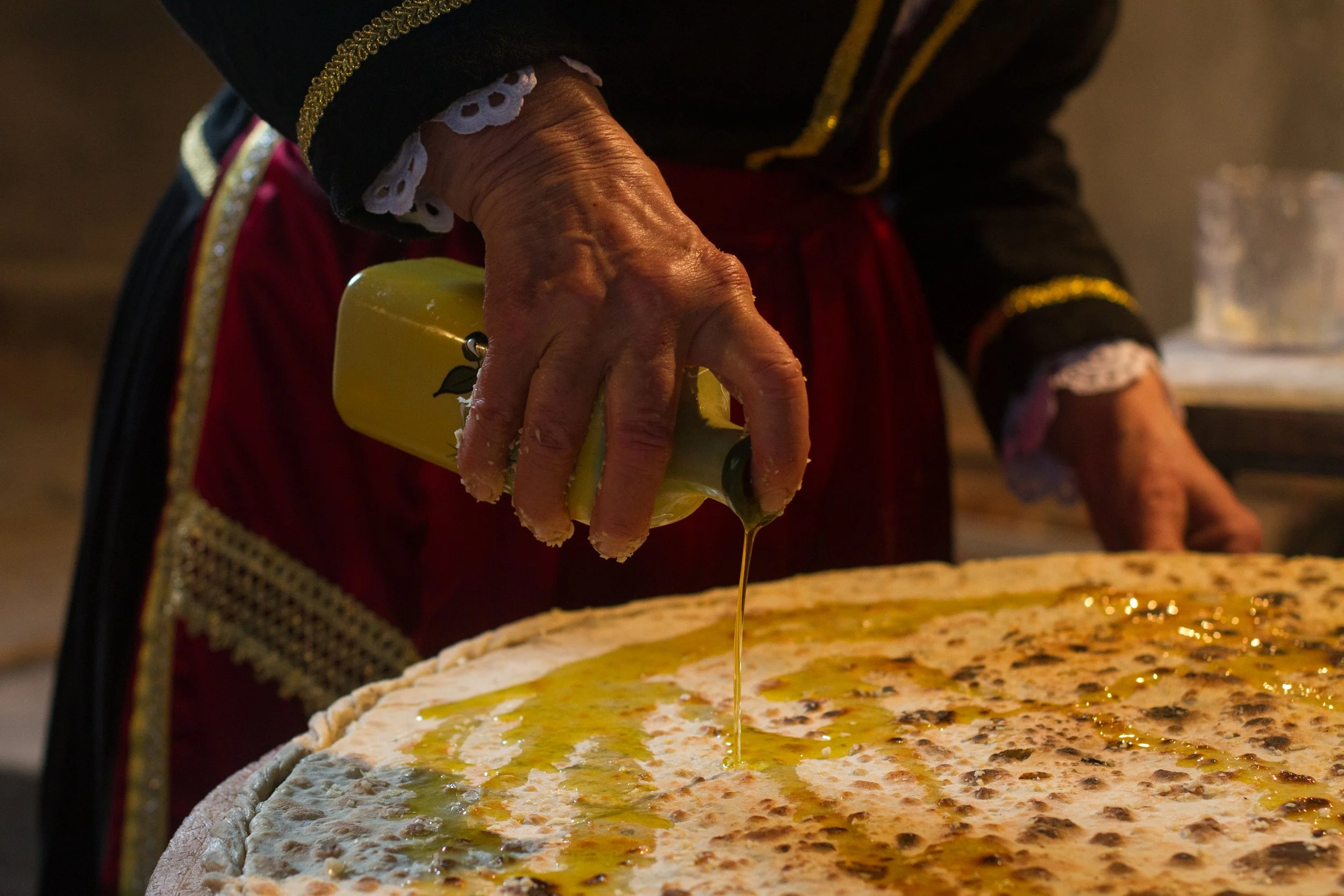 An elderly local woman's hands drizzling golden olive oil over traditional flatbread dough during a cooking class in the Konavle Valley near Dubrovnik, Croatia