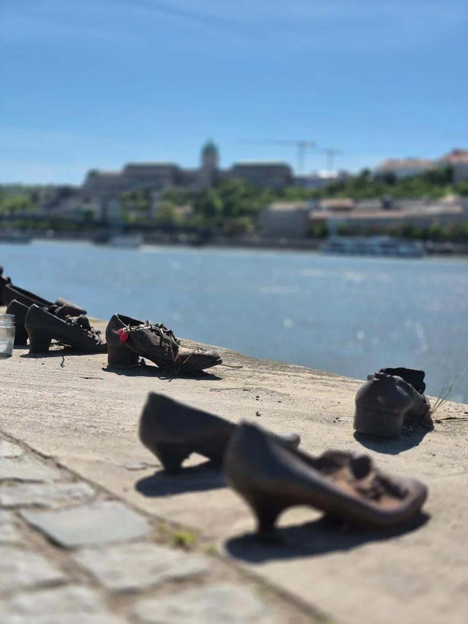 Cast iron shoes memorial on the bank of the Danube River in Budapest commemorating Jewish victims of the Holocaust, with the Buda hills visible across the water