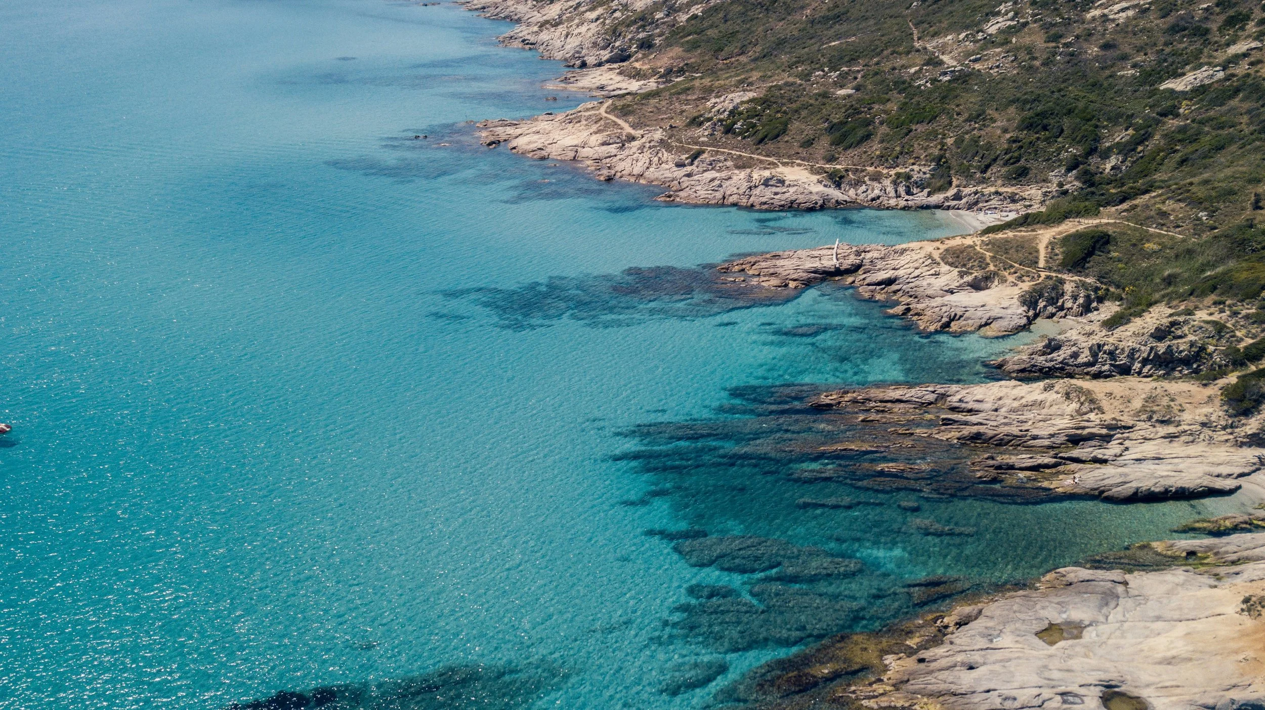 Aerial view of the turquoise Mediterranean water lapping against the rocky coastline of the French Riviera, France, with a coastal path visible above the sea
