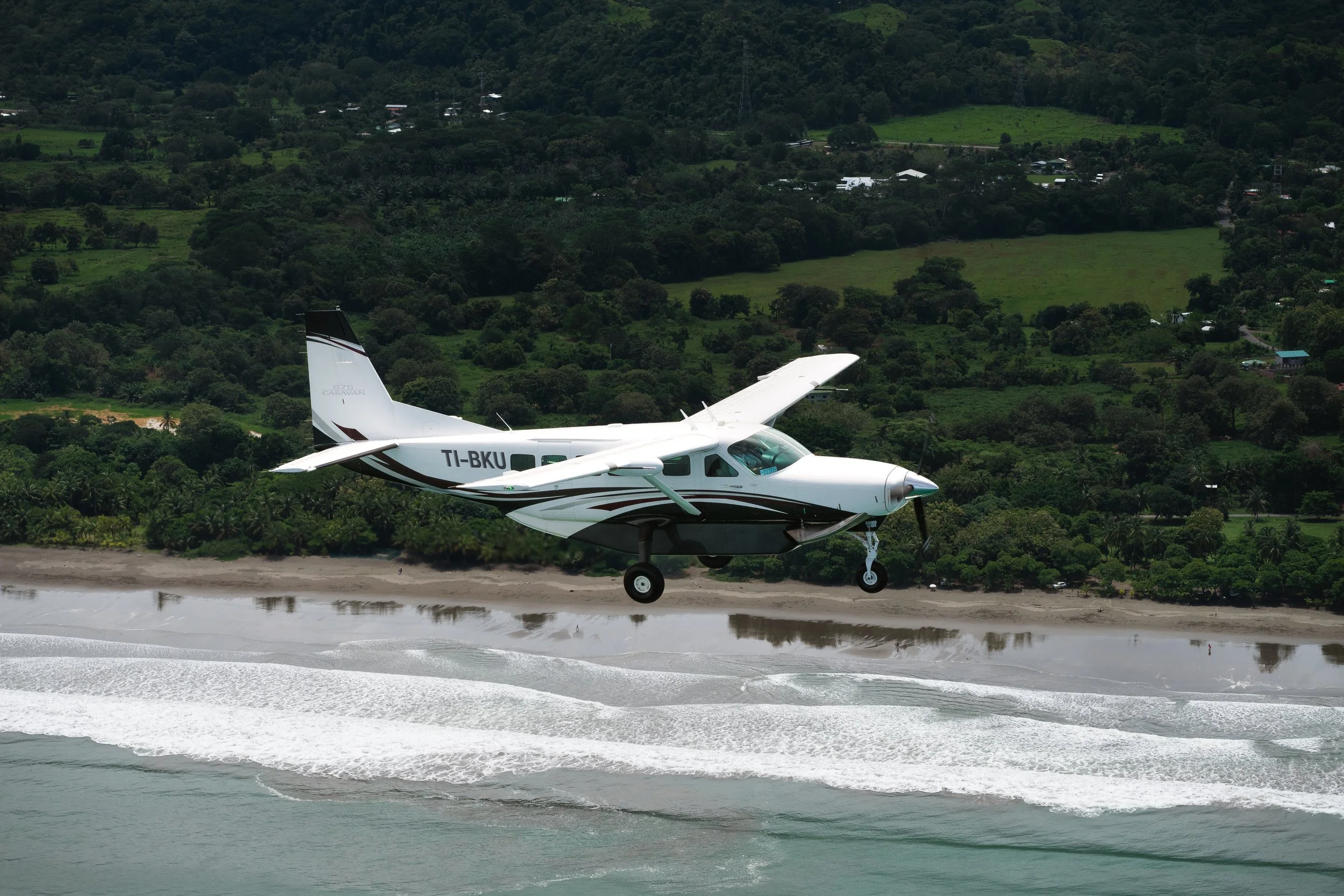 Small private plane landing on a coastal airstrip beside the ocean and jungle-covered hills in Costa Rica