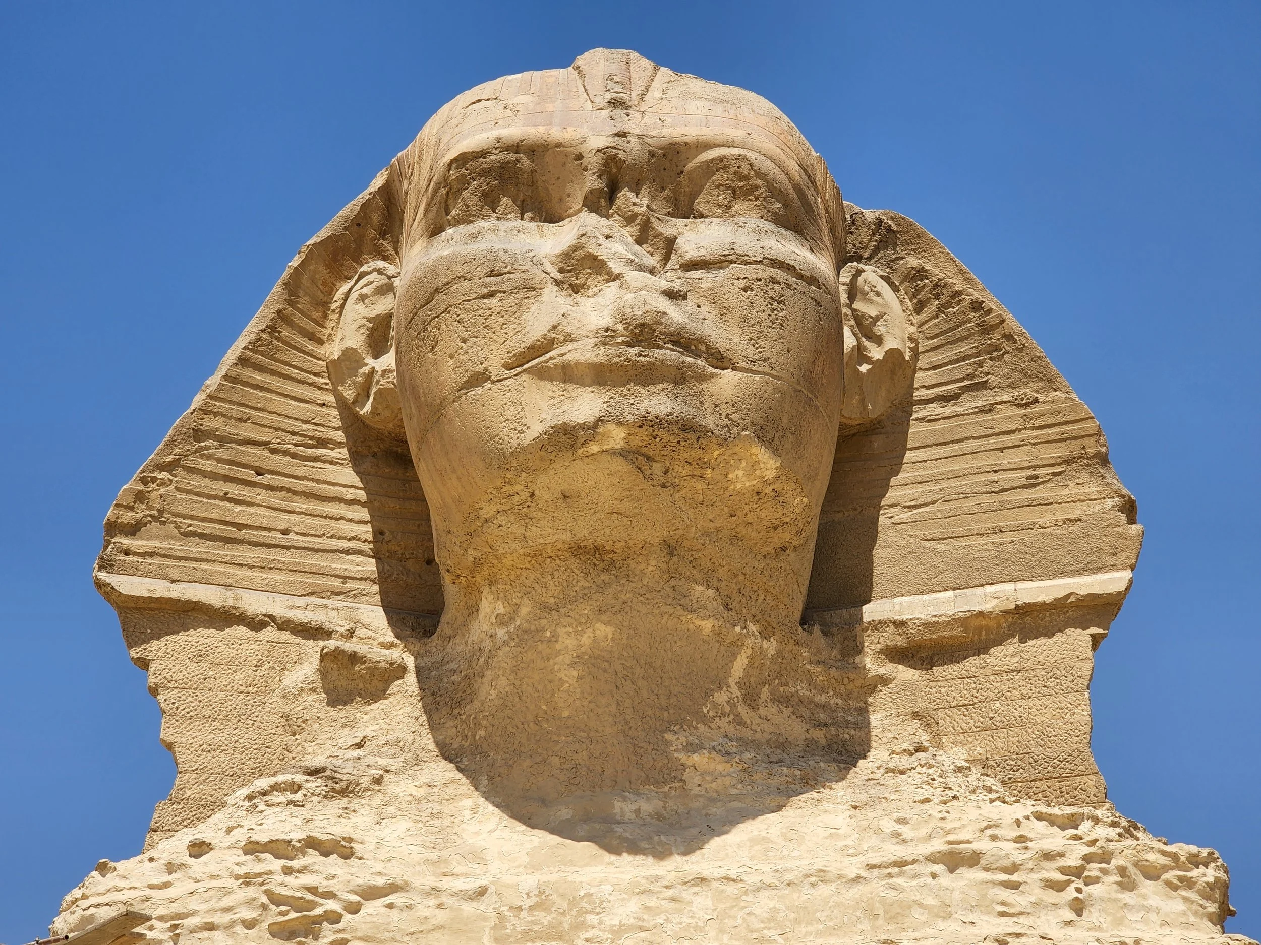 Close-up of the weathered limestone face of the Great Sphinx of Giza against a clear blue sky, Egypt