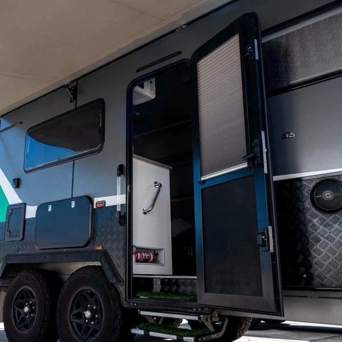 Open door of a modern black camper trailer with visible interior, including a metal handle and a fire extinguisher.
