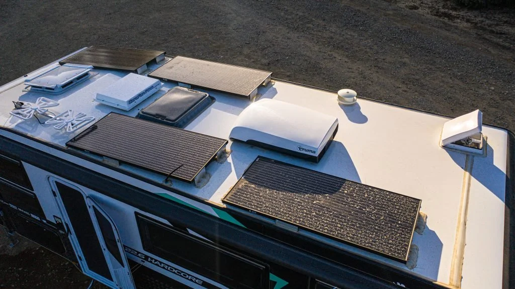 Top view of an RV roof with multiple solar panels and a ventilation unit.