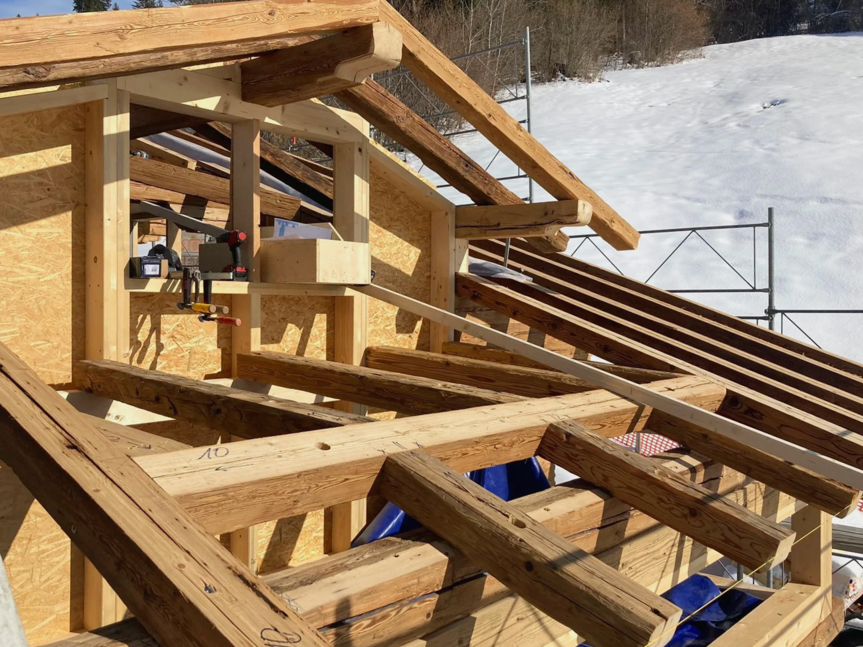 Wooden framing for a building under construction with snow-covered ground and trees in the background.