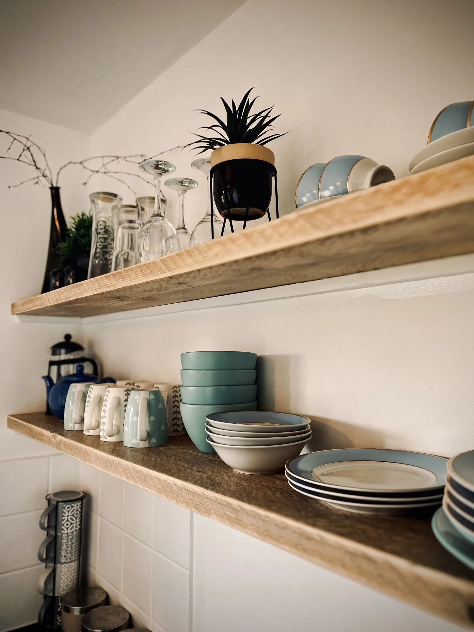 Wooden shelves holding glassware, plates, bowls, and a small potted plant in a black and beige pot.