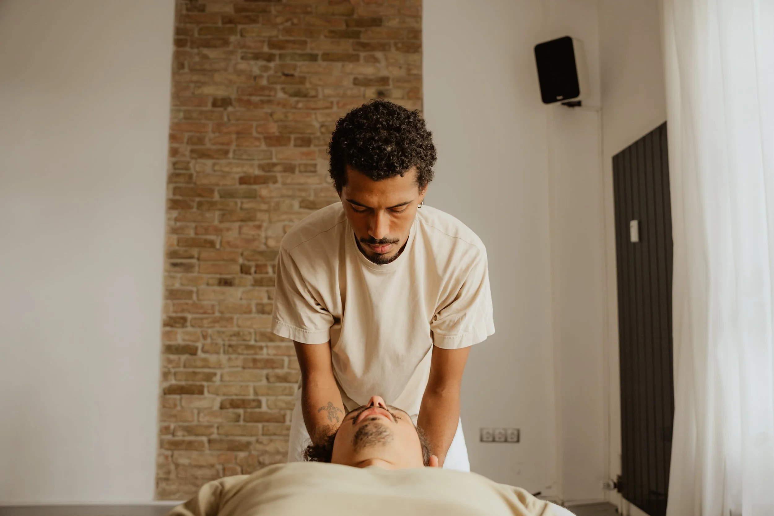Ein Masseur gibt einem Kunden eine Nackenmassage in einem Raum mit Steinwand und Vorhängen.