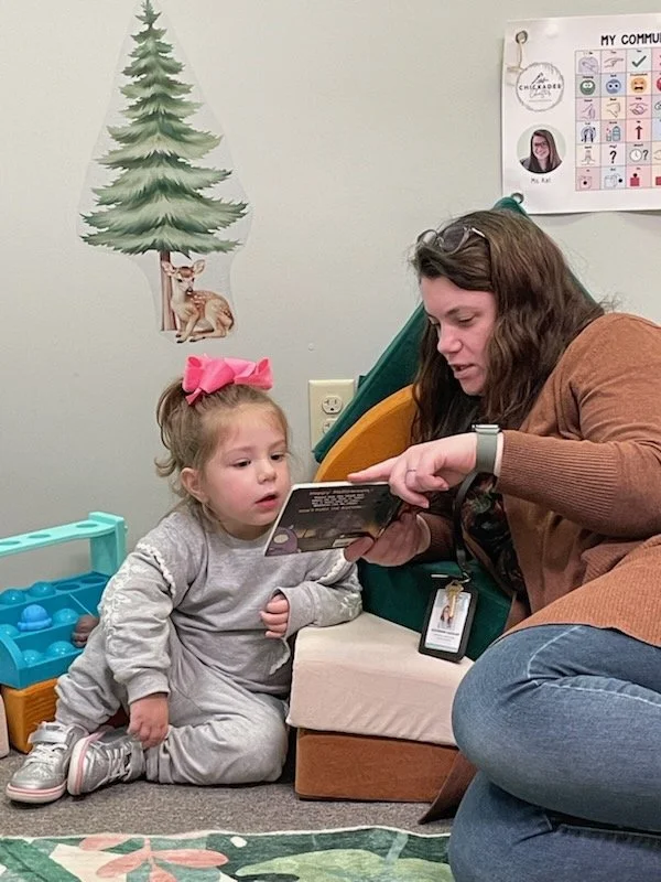 Speech Therapist reading a story to toddler on a comfy couch in the woodland-theme clinic space.