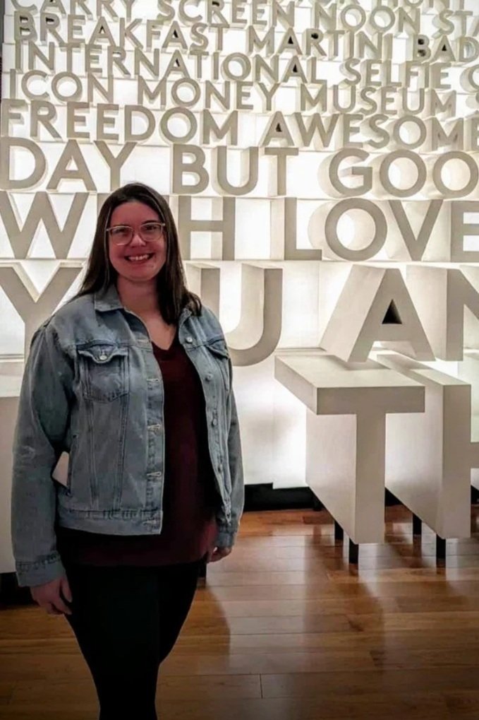 Lisa, a speech clinician, standing in front a wall of brightly lit words.