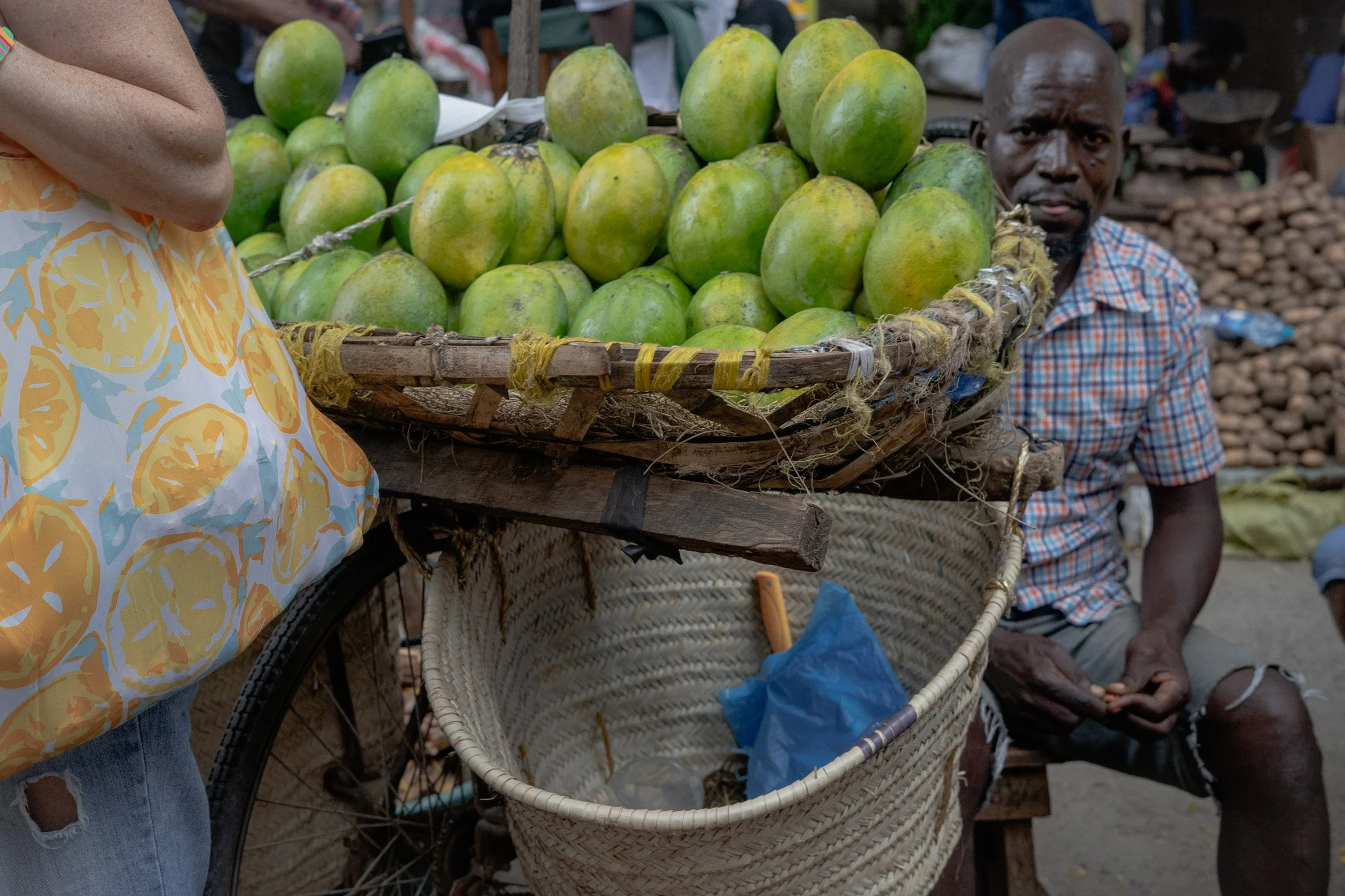 A man sitting near a cart filled with green papayas at an outdoor market.