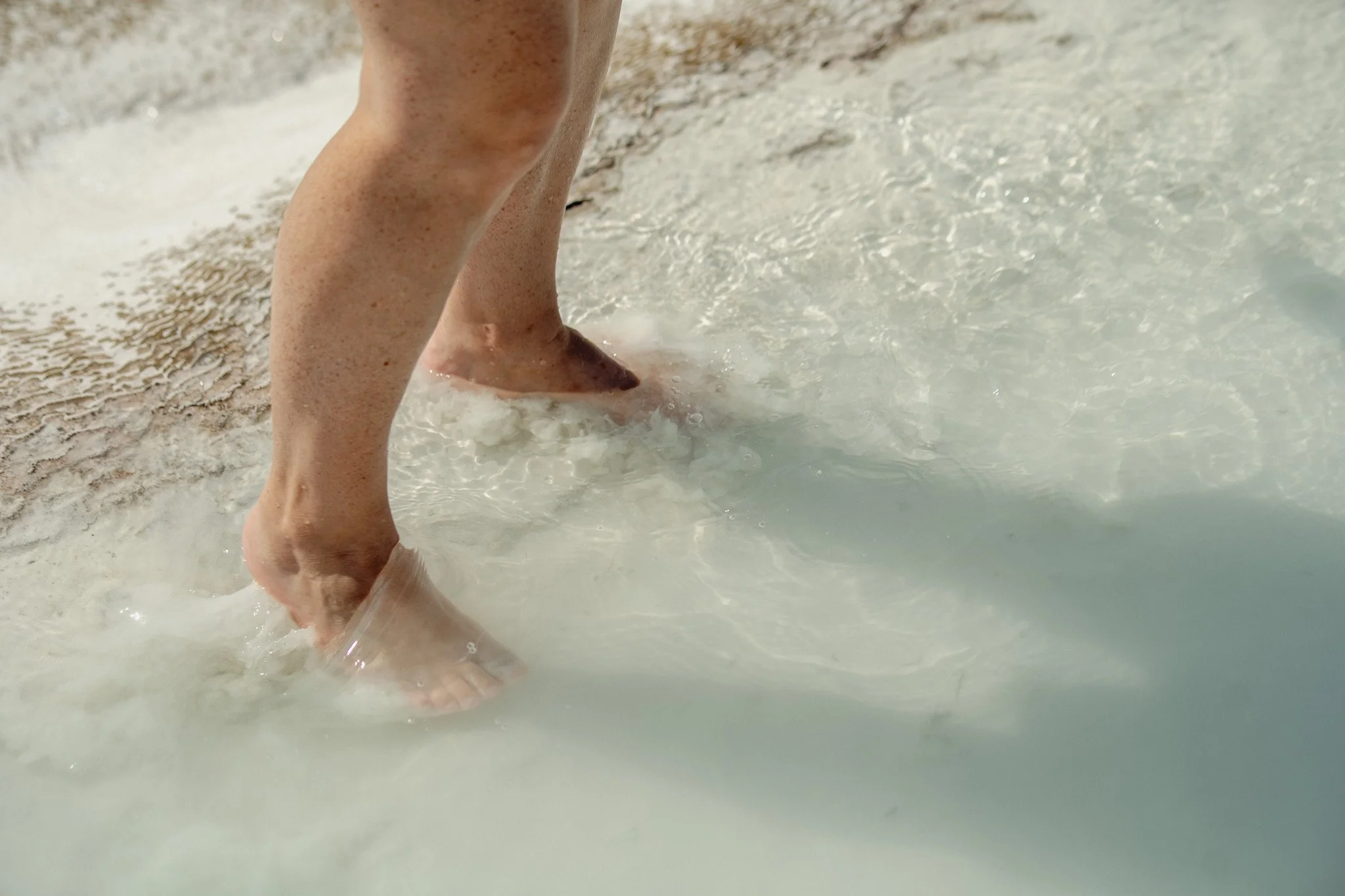 Close-up of a person's legs and feet in shallow water at the beach.