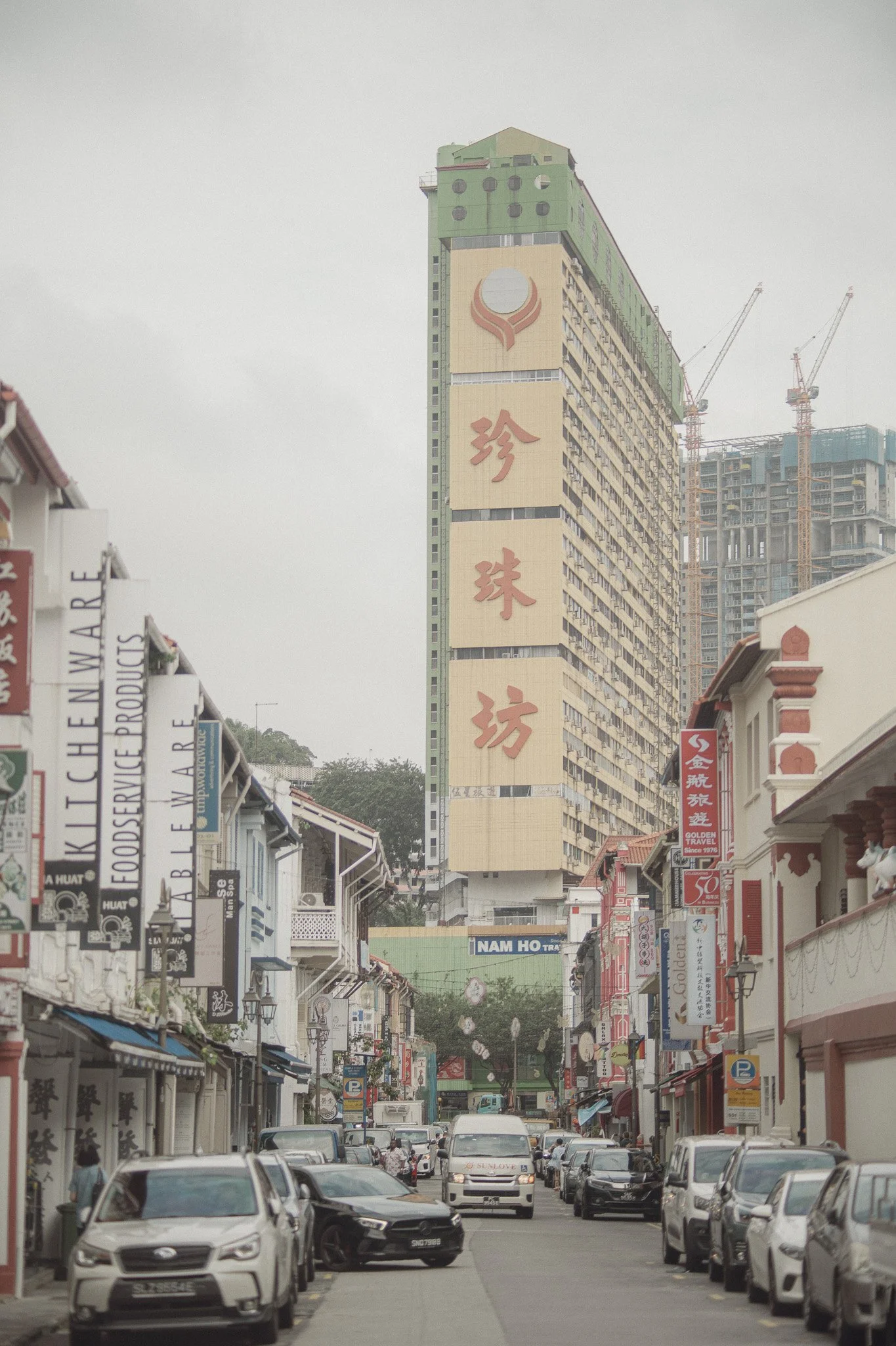 A busy street scene in Chinatown, featuring traditional shopfronts on both sides and a tall building with Chinese characters on its facade in the background.
