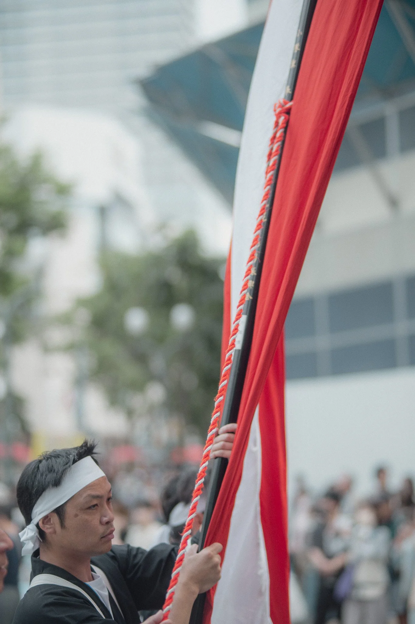 Person holding a flag at a public event or parade, with a crowd and buildings in the background.