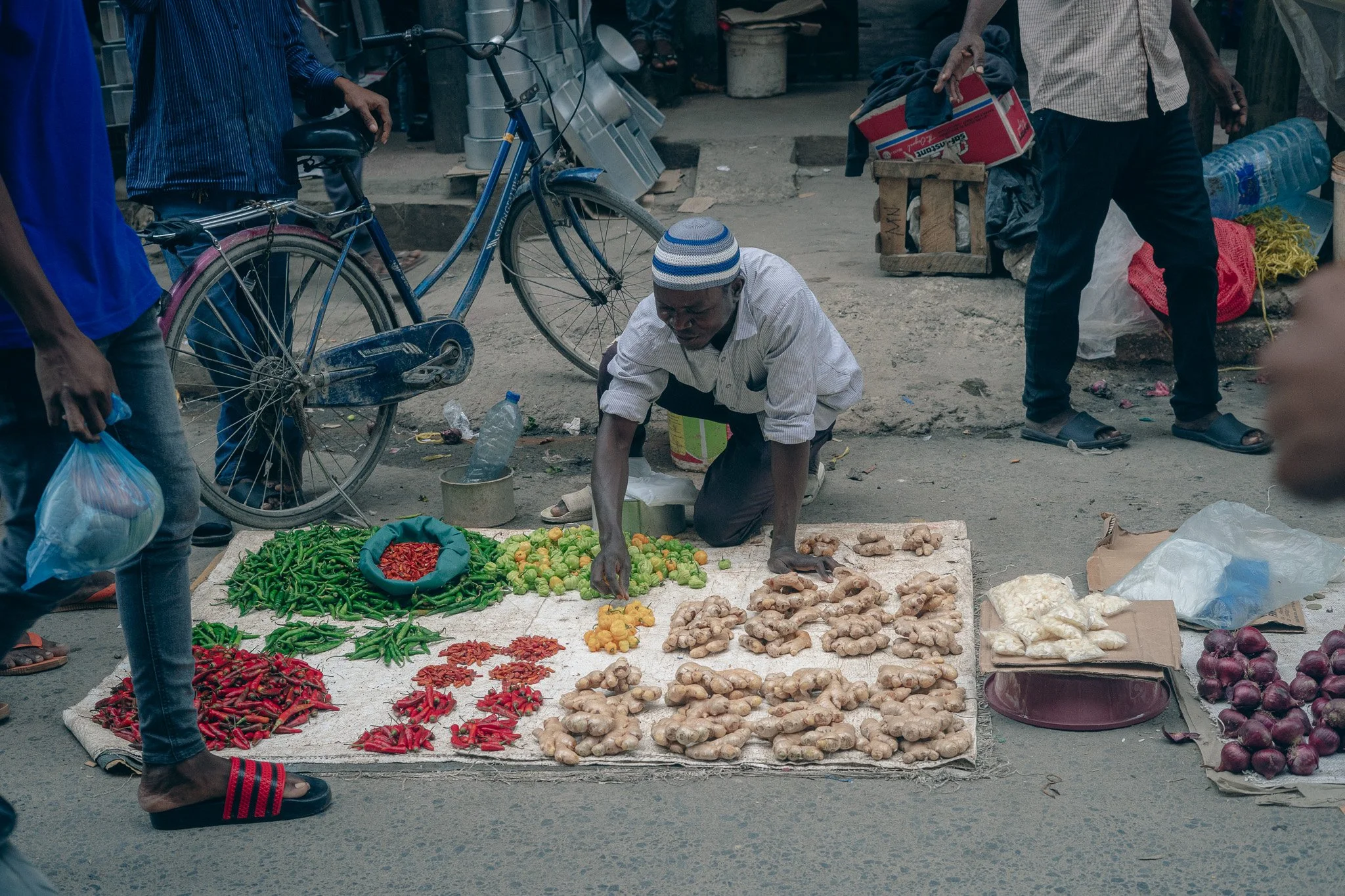 Street vendor selling fresh ginger, chili peppers, and onions at an outdoor market.