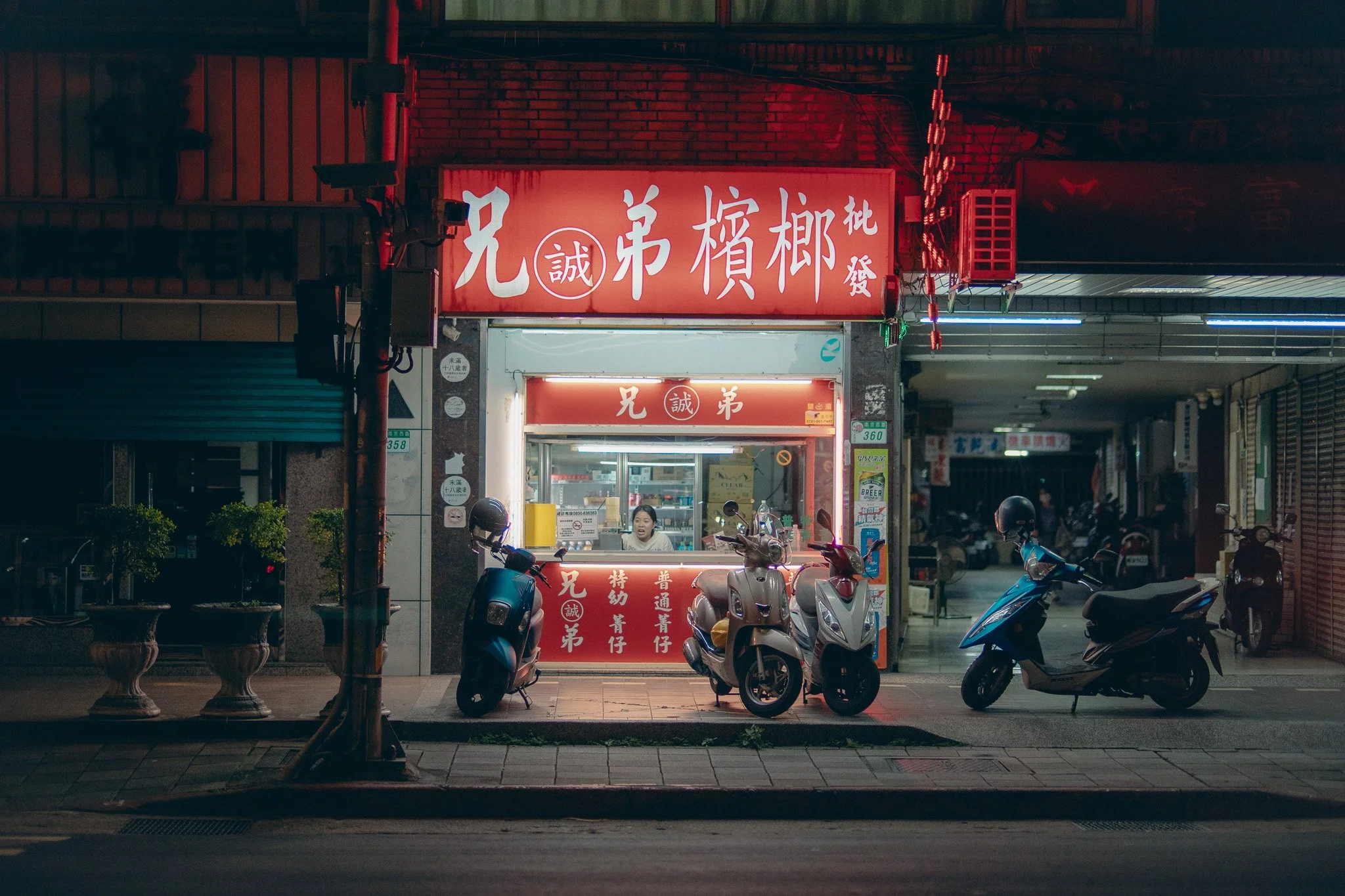 Night view of a small Asian food stall with red signage and parked scooters in front.