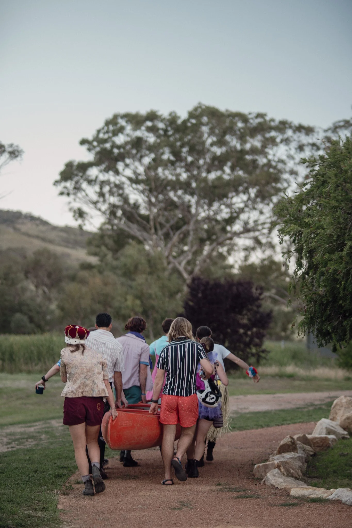 People walking on a dirt path through a park near trees and grassy fields during daytime.