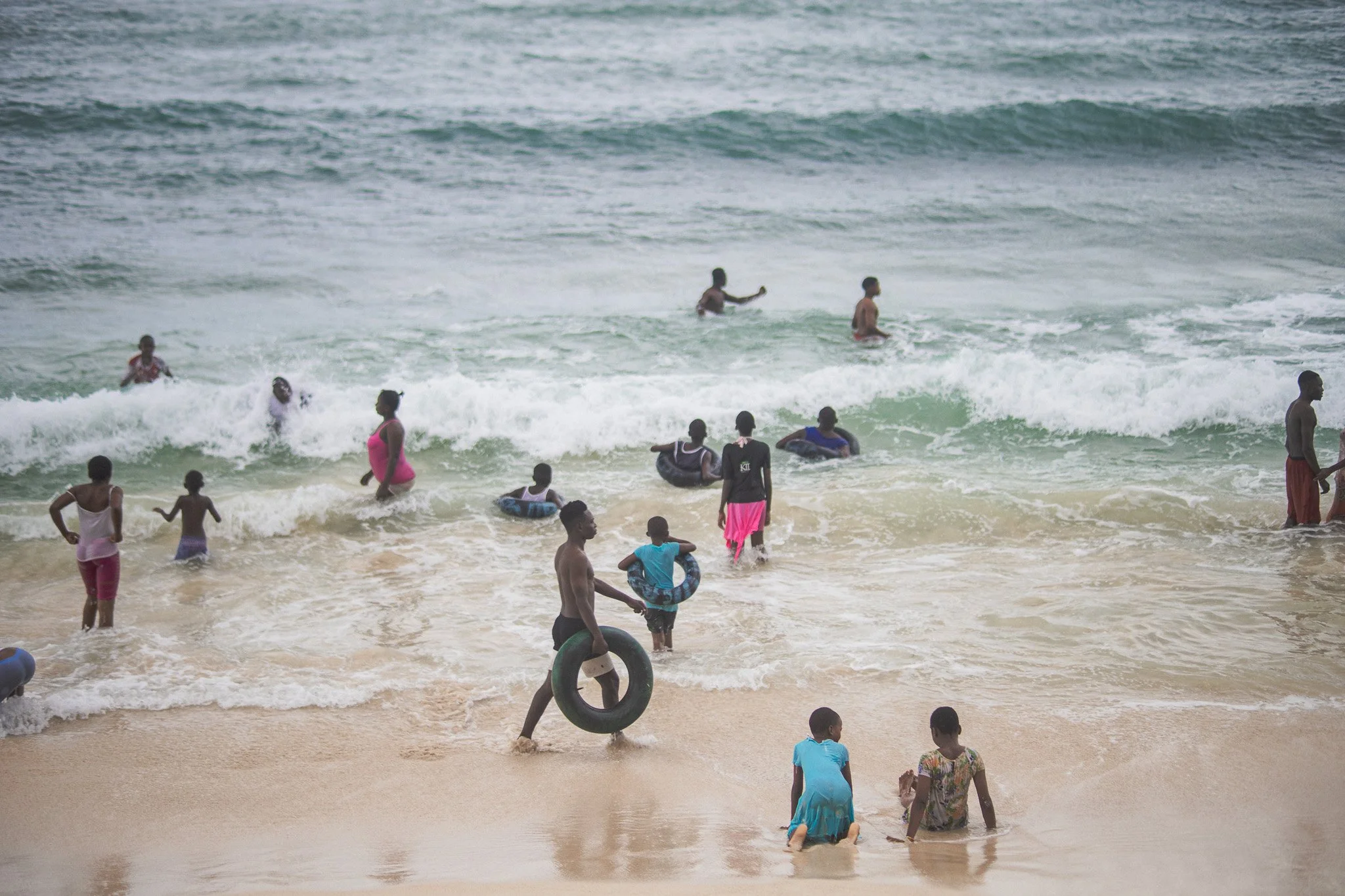 People, including children and adults, enjoying a day at the beach with some swimming and playing in the water and sand.
