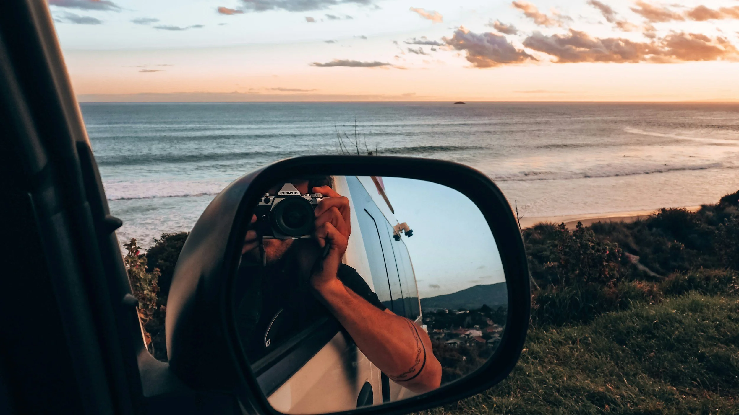 Photographer reflected in car side mirror with ocean view
