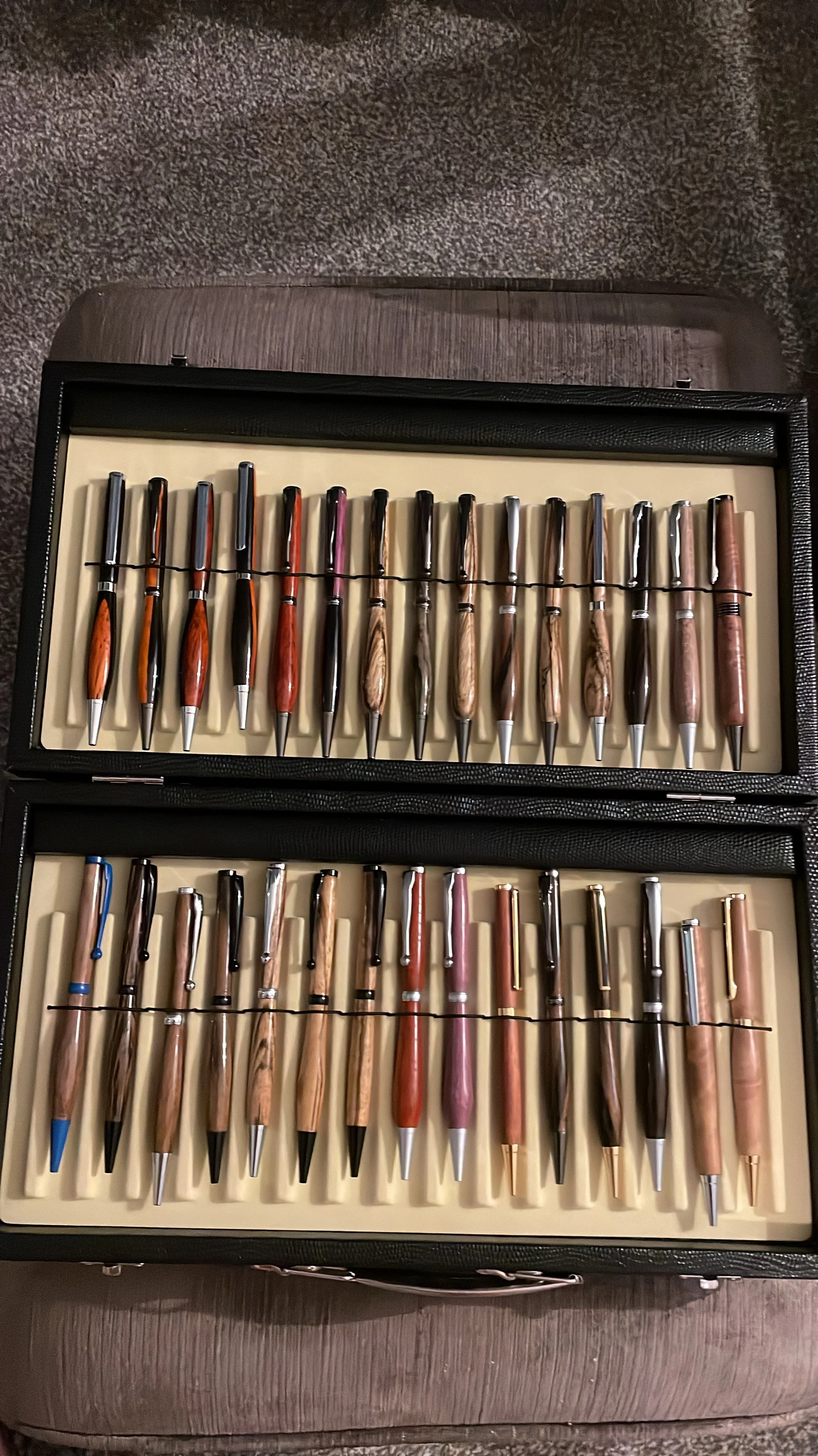 A collection of three sets of fountain pens in a display case, with various colors and wood finishes.