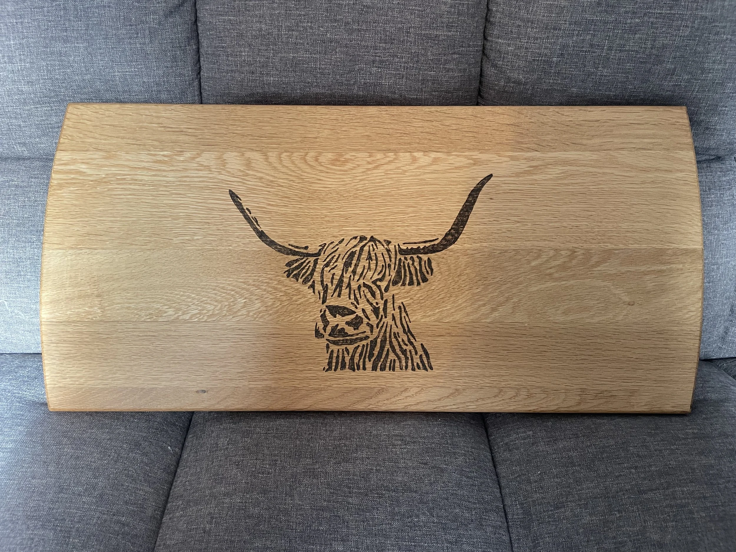 A wooden table with a black bull skull design burned into the surface, placed on a gray upholstered couch.
