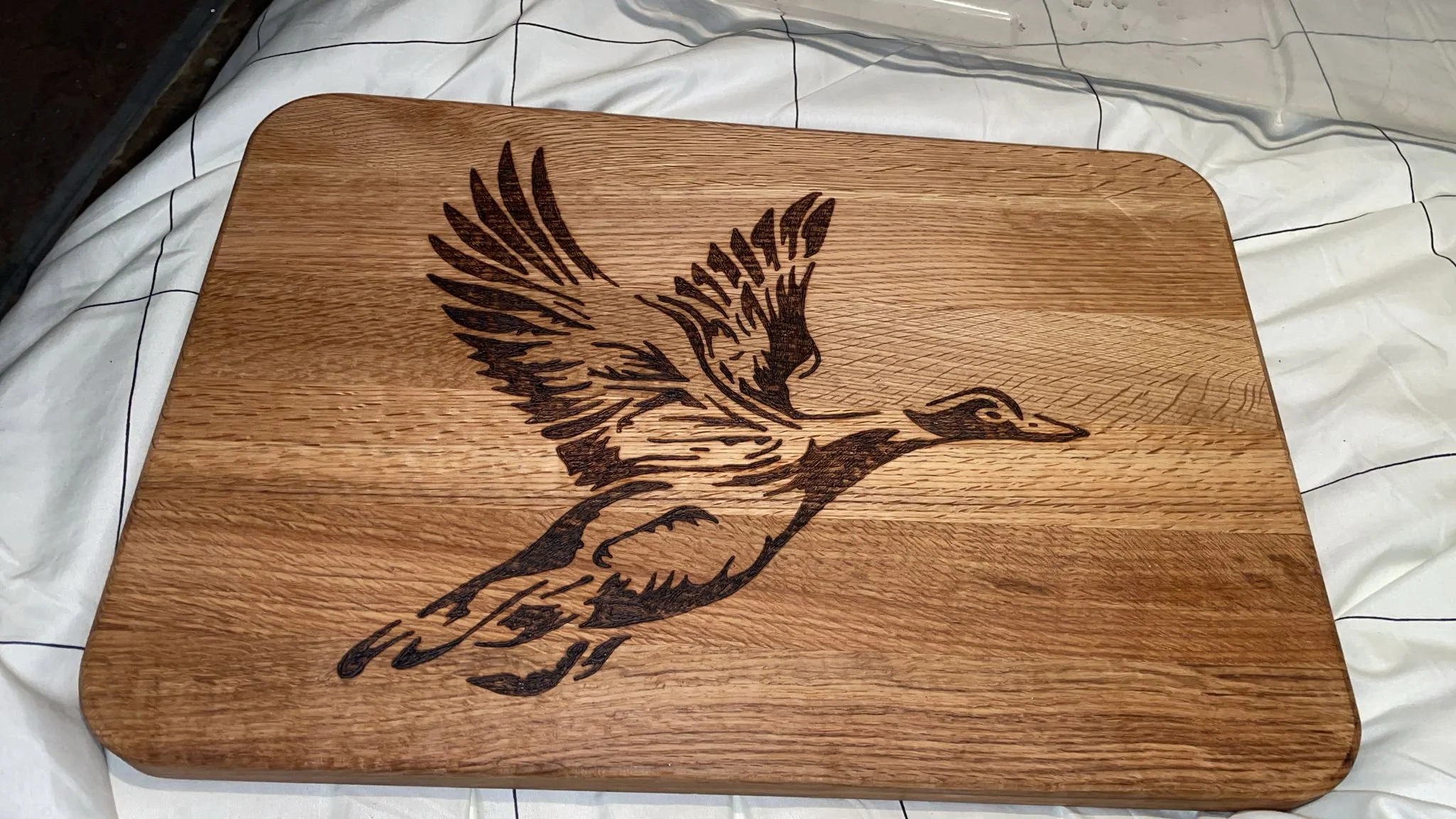A wooden cutting board with an engraved image of a duck with wings spread.