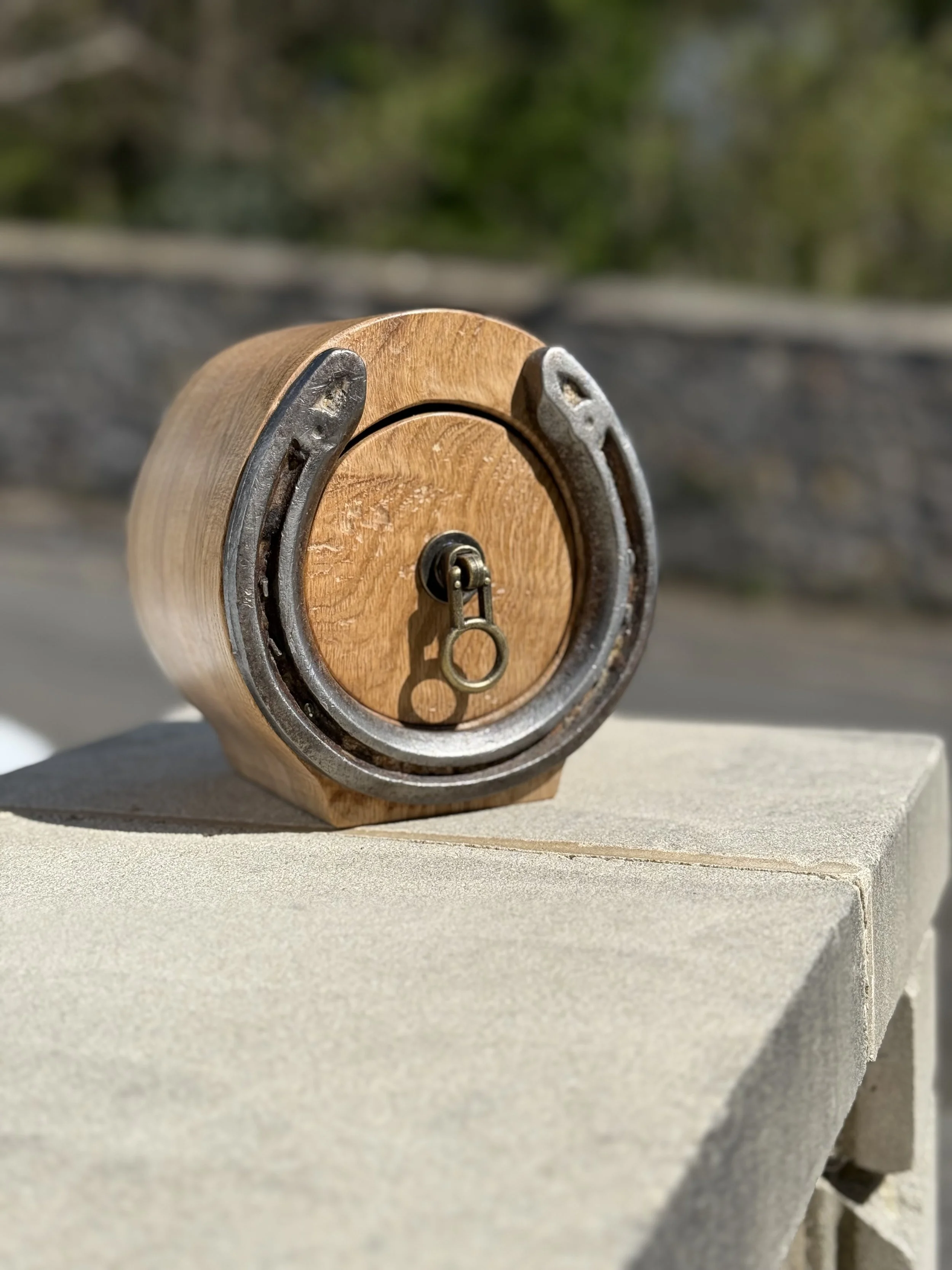 A wooden and metal toy drum with a drum key, placed on a concrete surface outdoors.