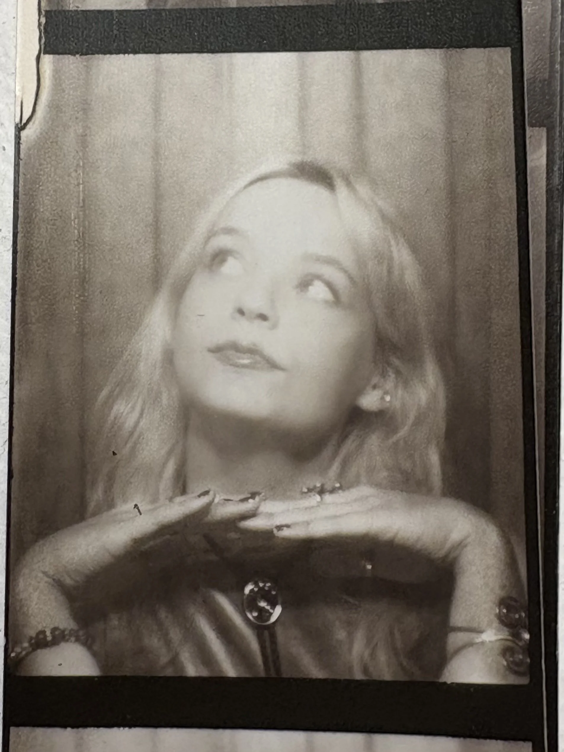 Black and white photo of a woman with wavy hair resting her chin on her hands, looking thoughtfully at the camera.